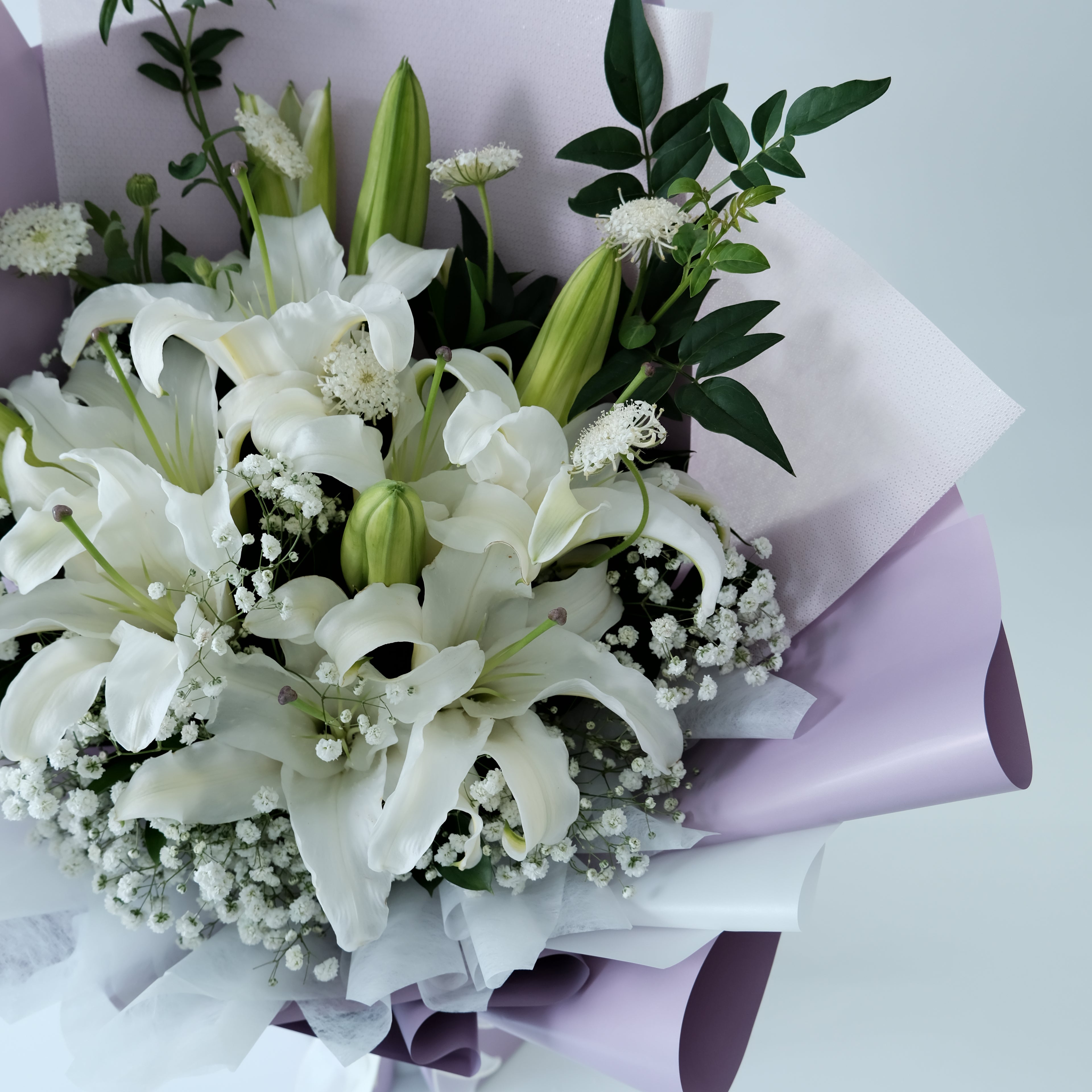 Bouquet of white lilies and greenery on a light background