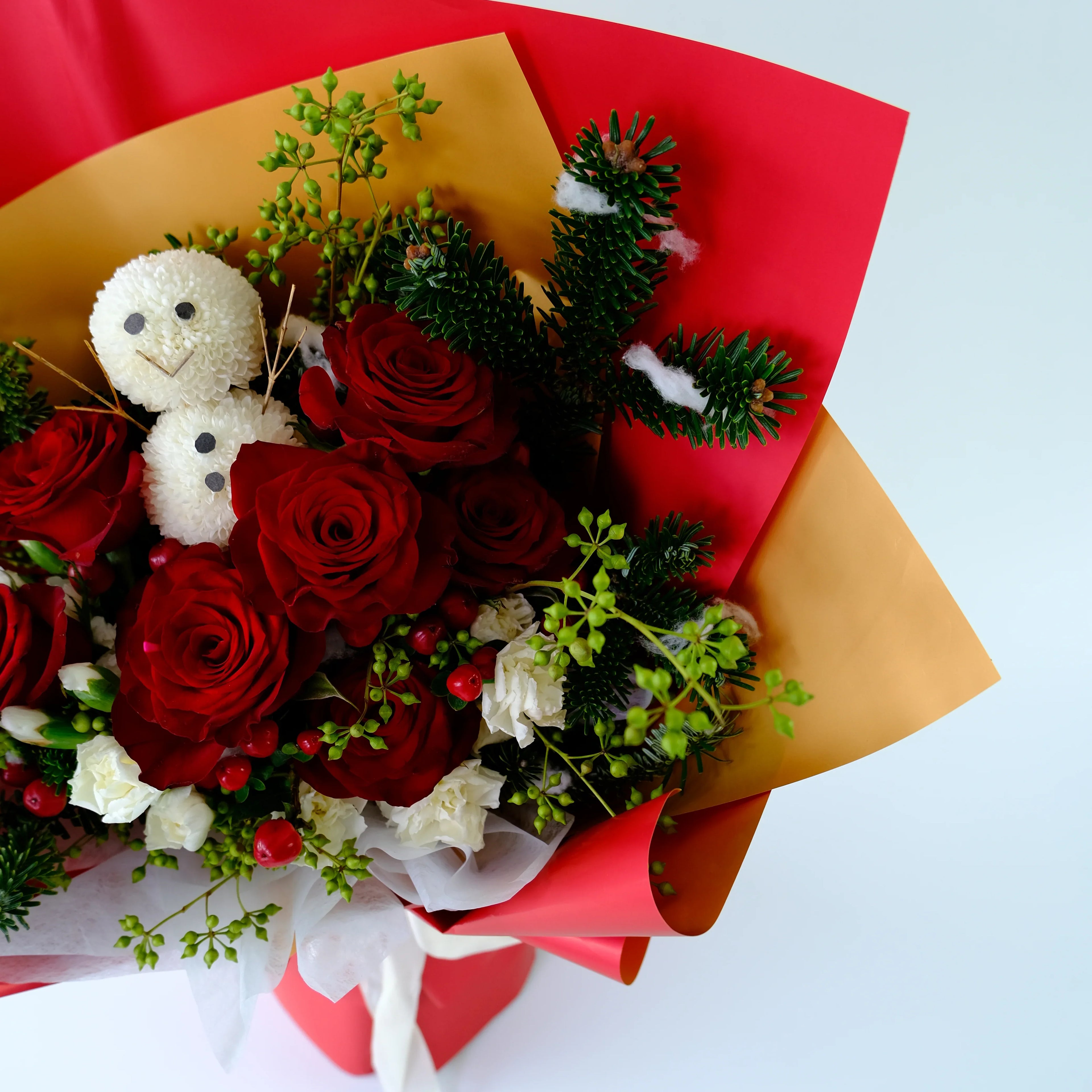 Christmas bouquet with red roses, white flowers, snowman decoration and festive greenery.