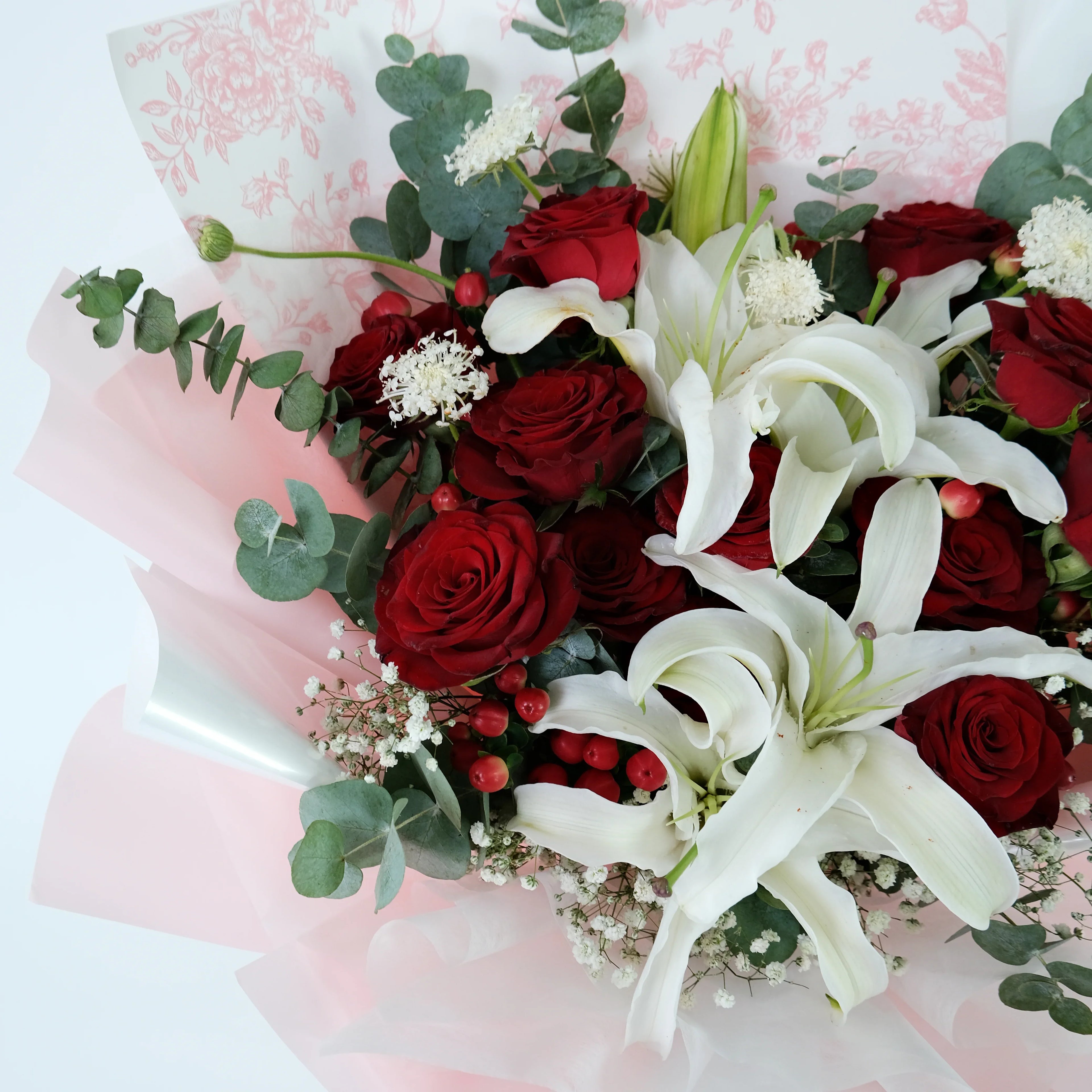 Bouquet of red roses and white lilies wrapped in pink floral paper