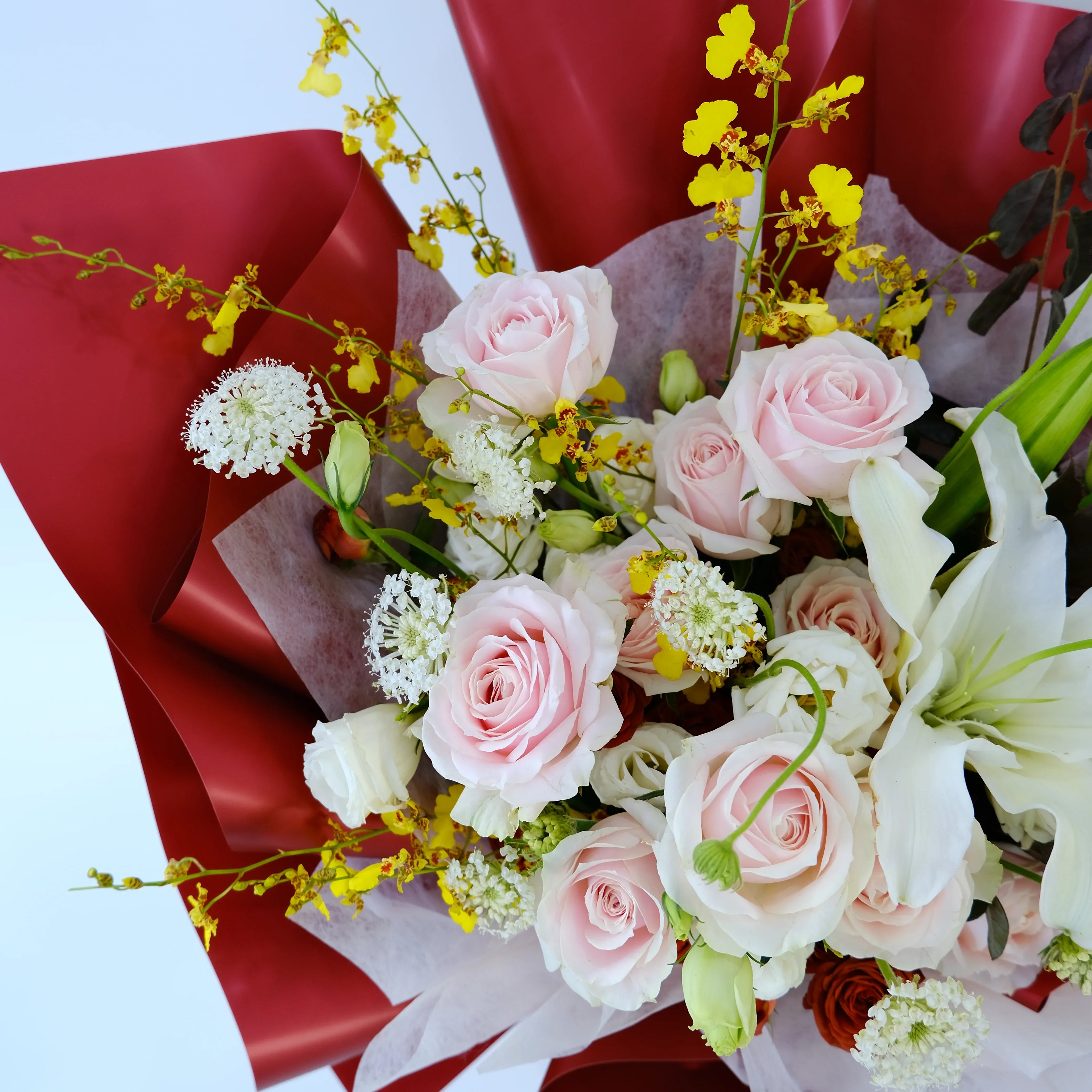 Bouquet with pink roses, white lilies, yellow flowers, red wrap