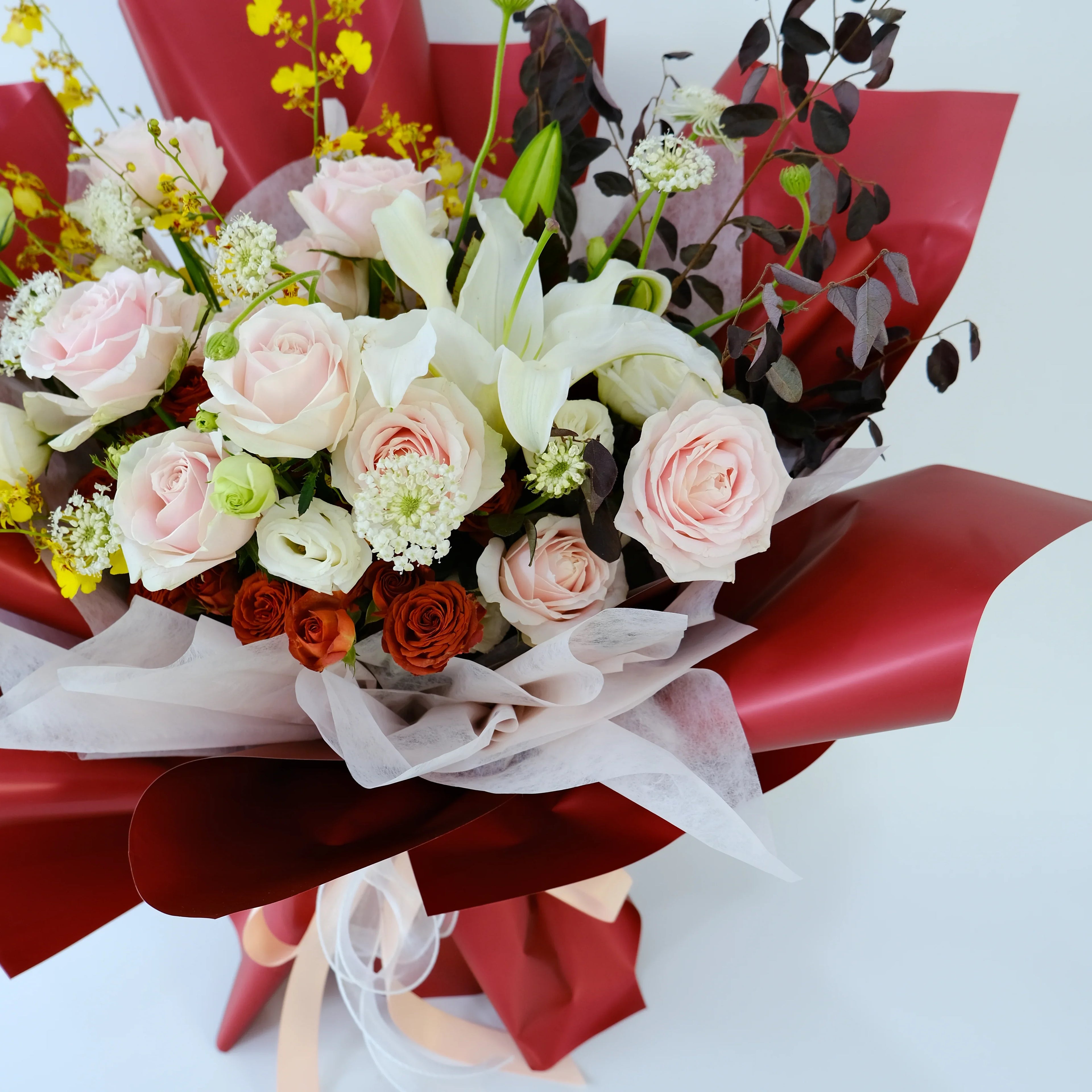 Elegant bouquet of pink roses, white lilies, and red flowers wrapped in red paper