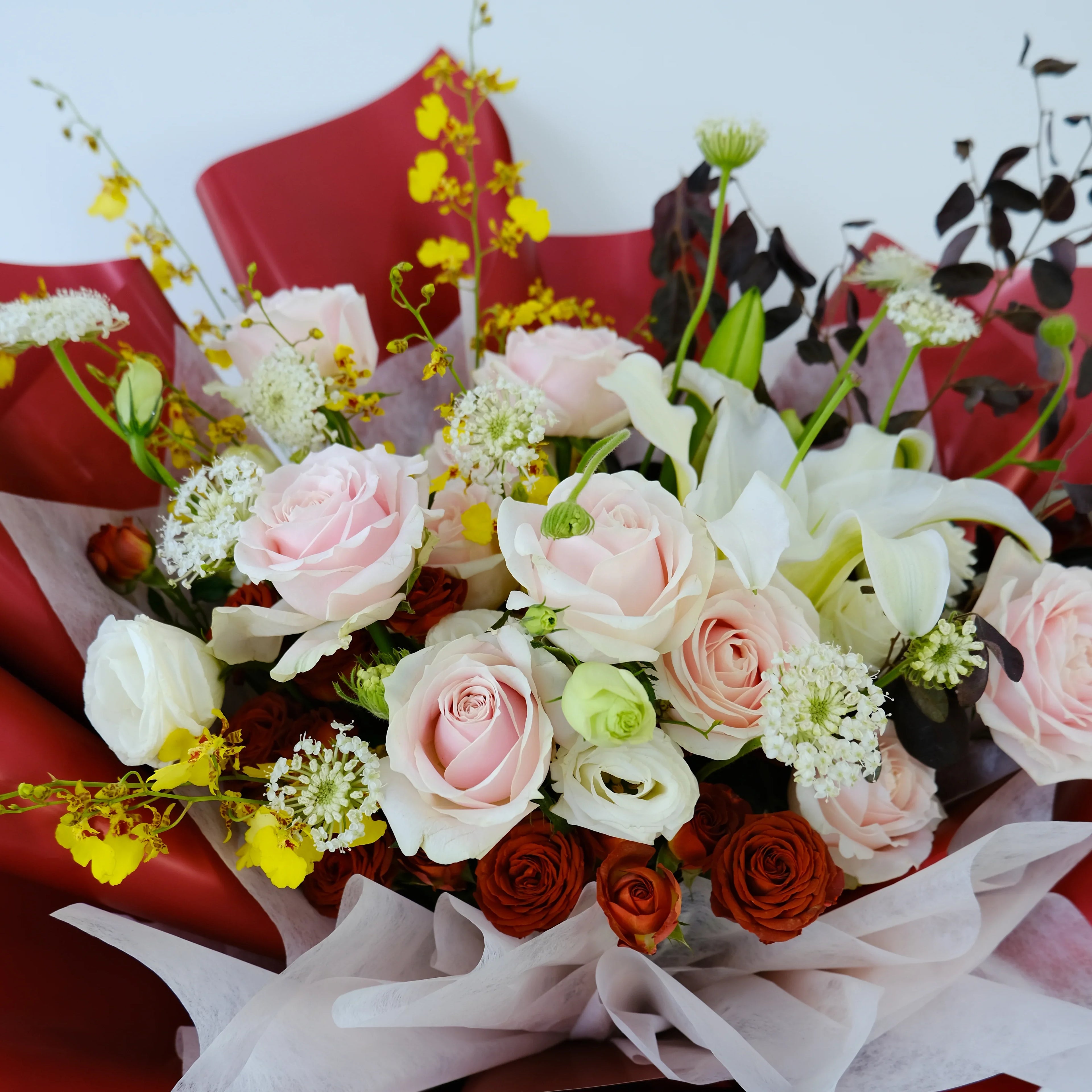 Elegant bouquet with pink roses, white lilies, yellow flowers and red wrapping