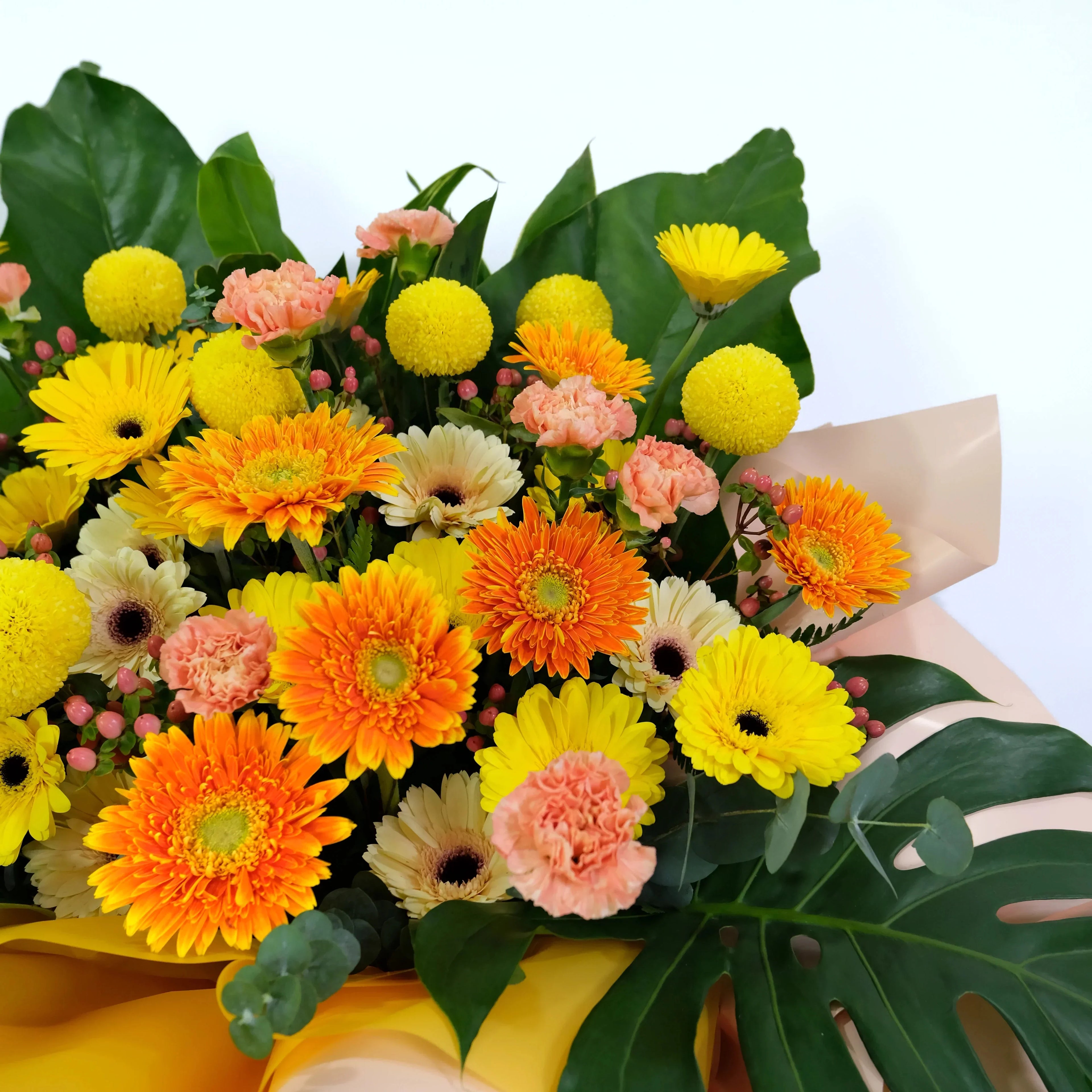 Bouquet of colorful flowers including yellow, orange, and pink flowers with green leaves on a light background.