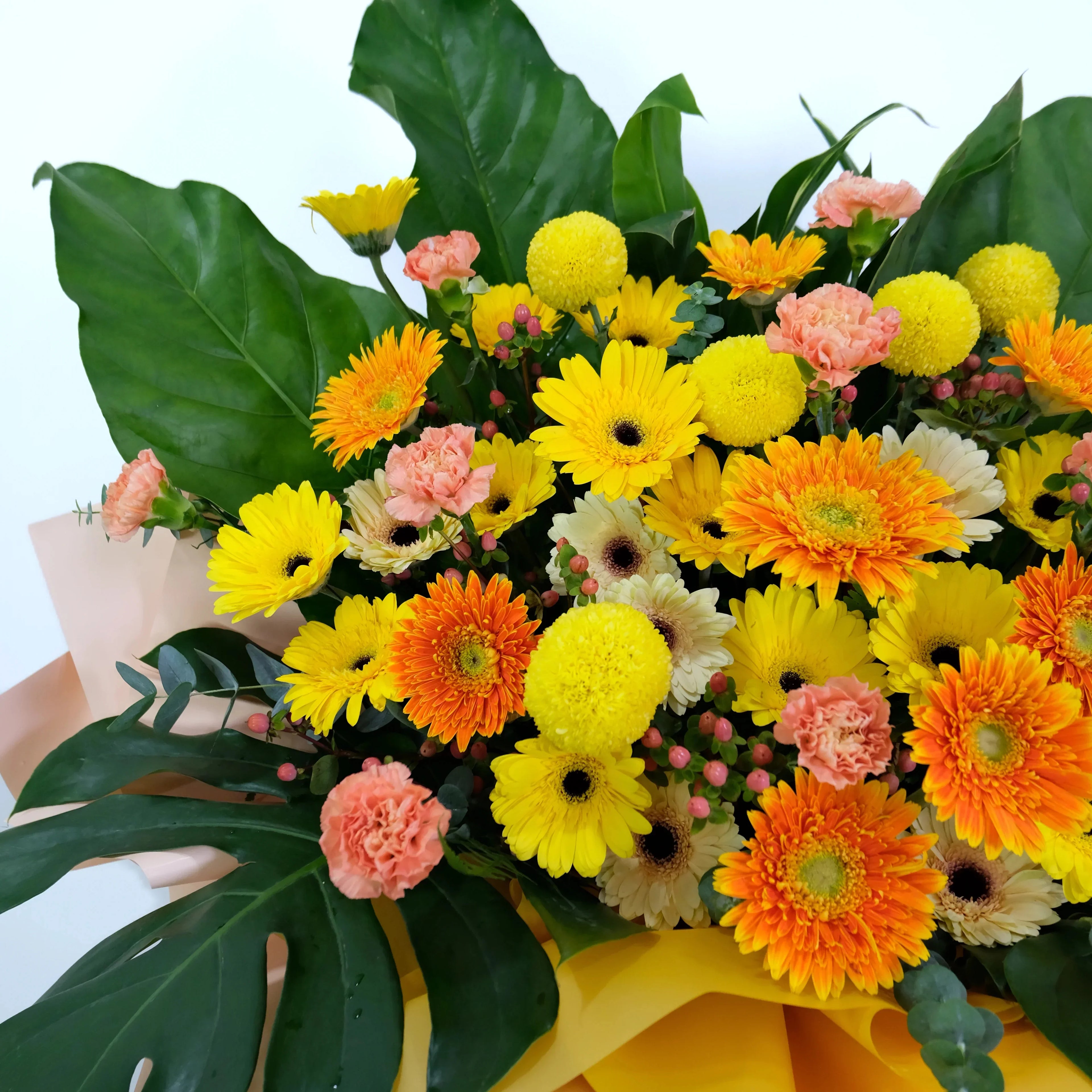 Bouquet of colorful flowers including yellow, orange, and pink flowers with green leaves.