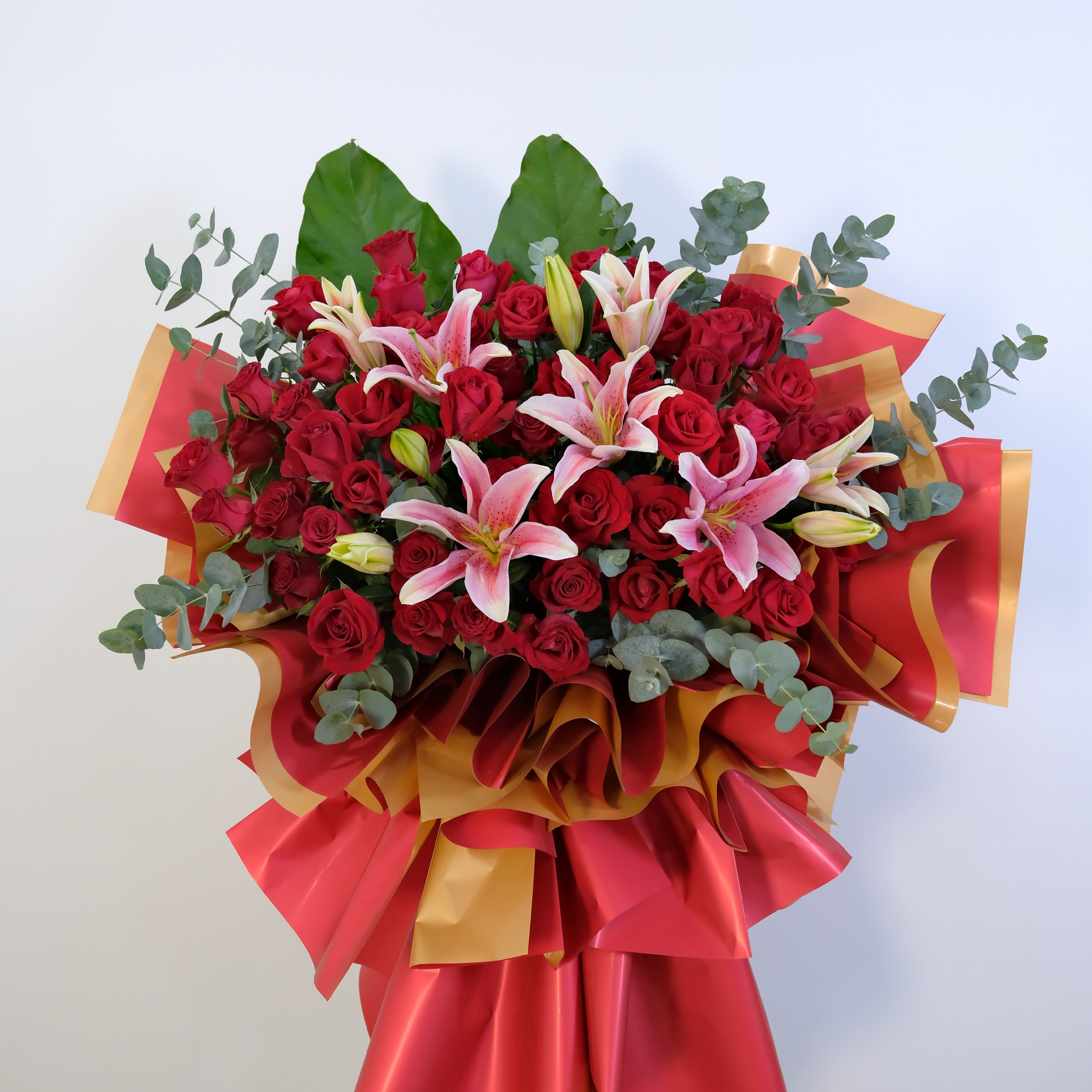 flower stand Bouquet of red roses and pink lilies with gold and red ribbons on a light background