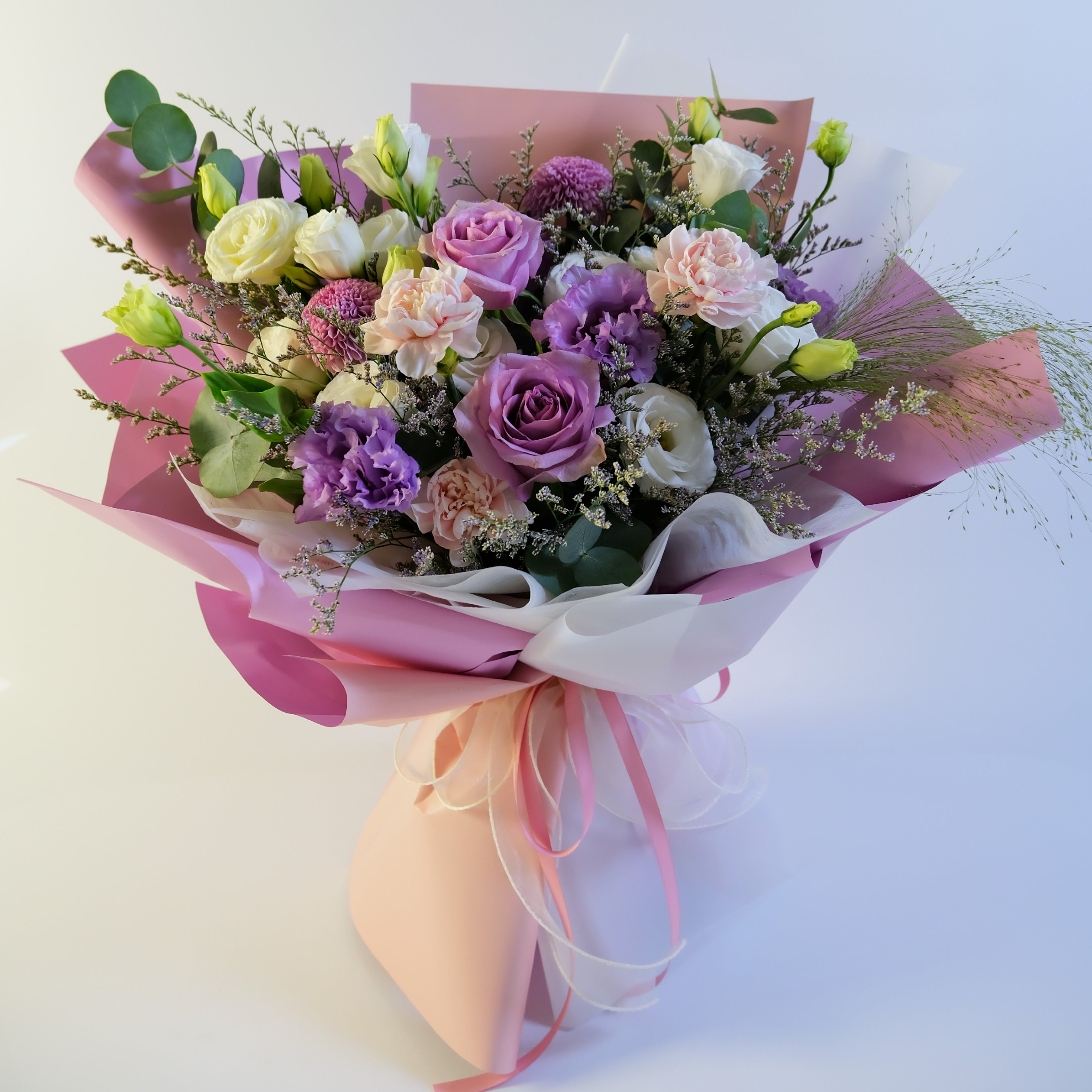 Bouquet of flowers wrapped in pink paper with a white ribbon on a light background