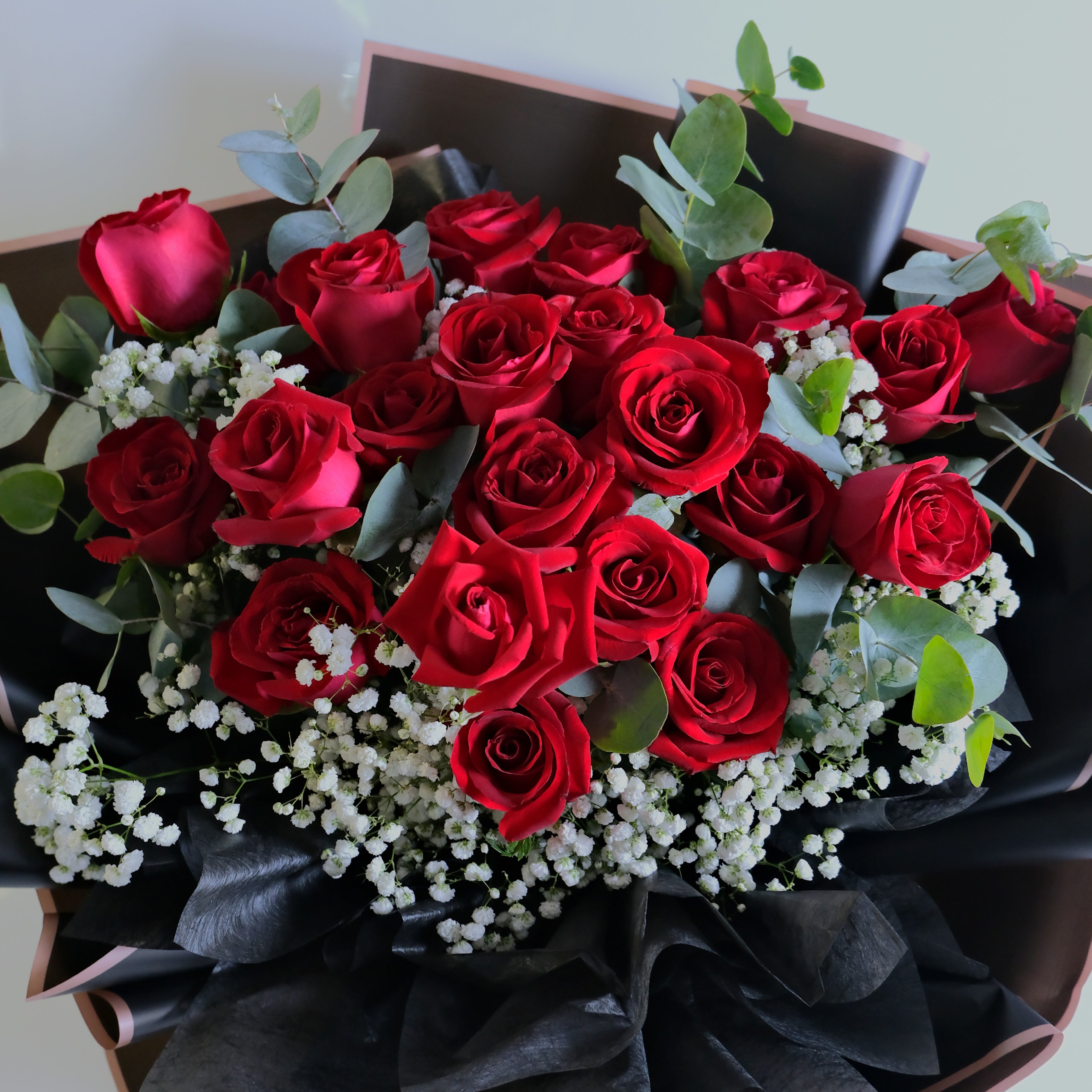Bouquet of red roses with greenery and white flowers in a black box.