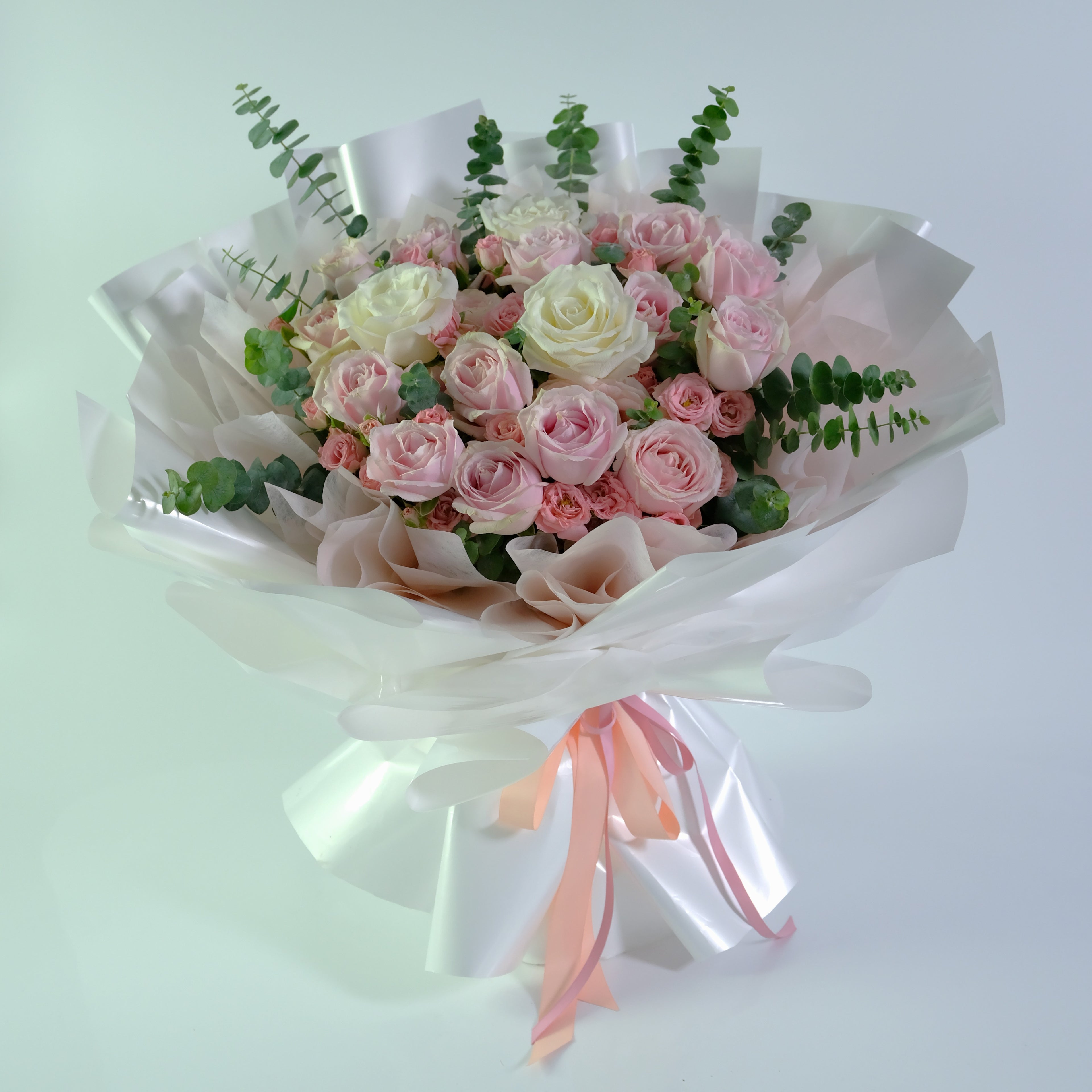 Bouquet of pink and white roses with greenery on a light background