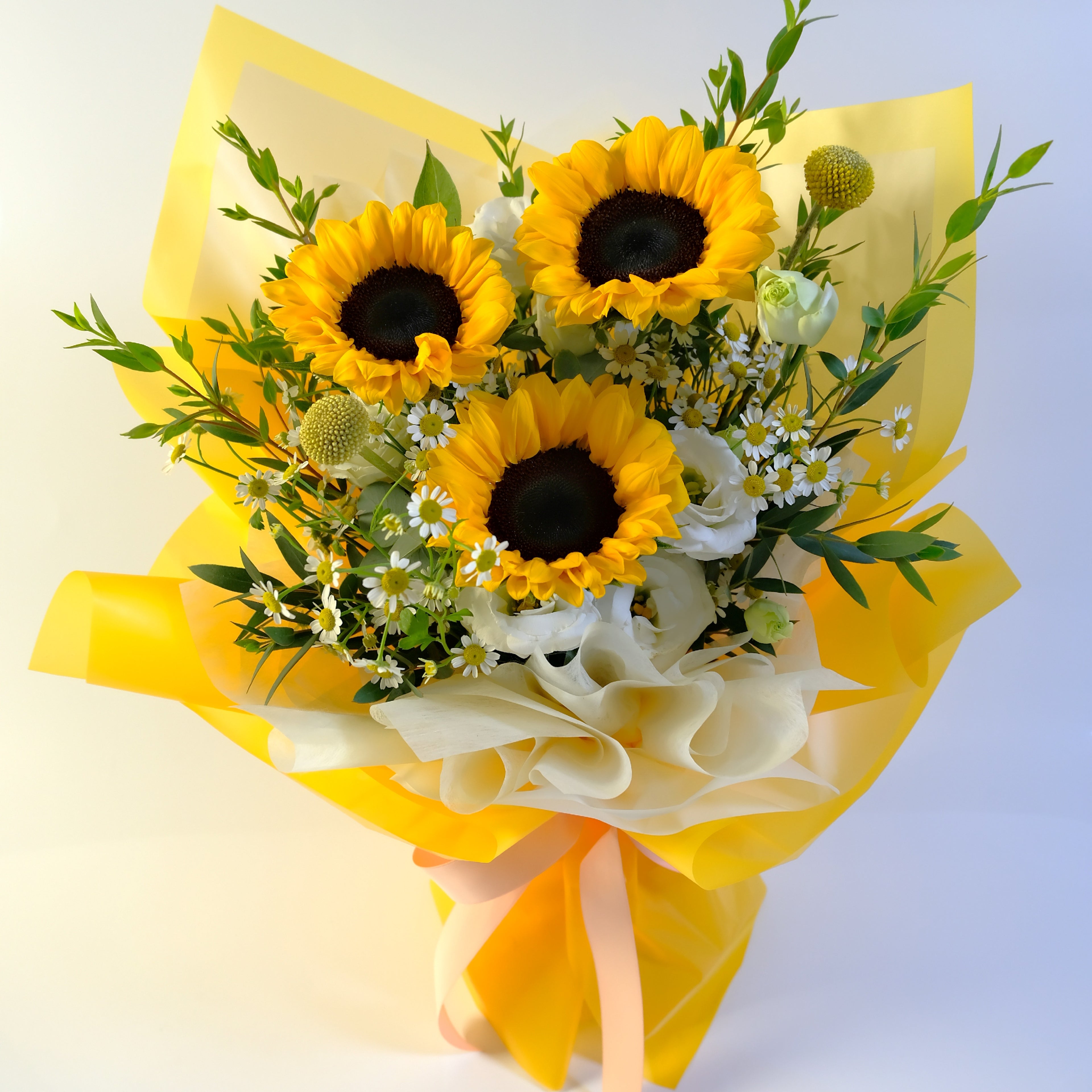 Bouquet of sunflowers and white flowers wrapped in yellow paper on a light background