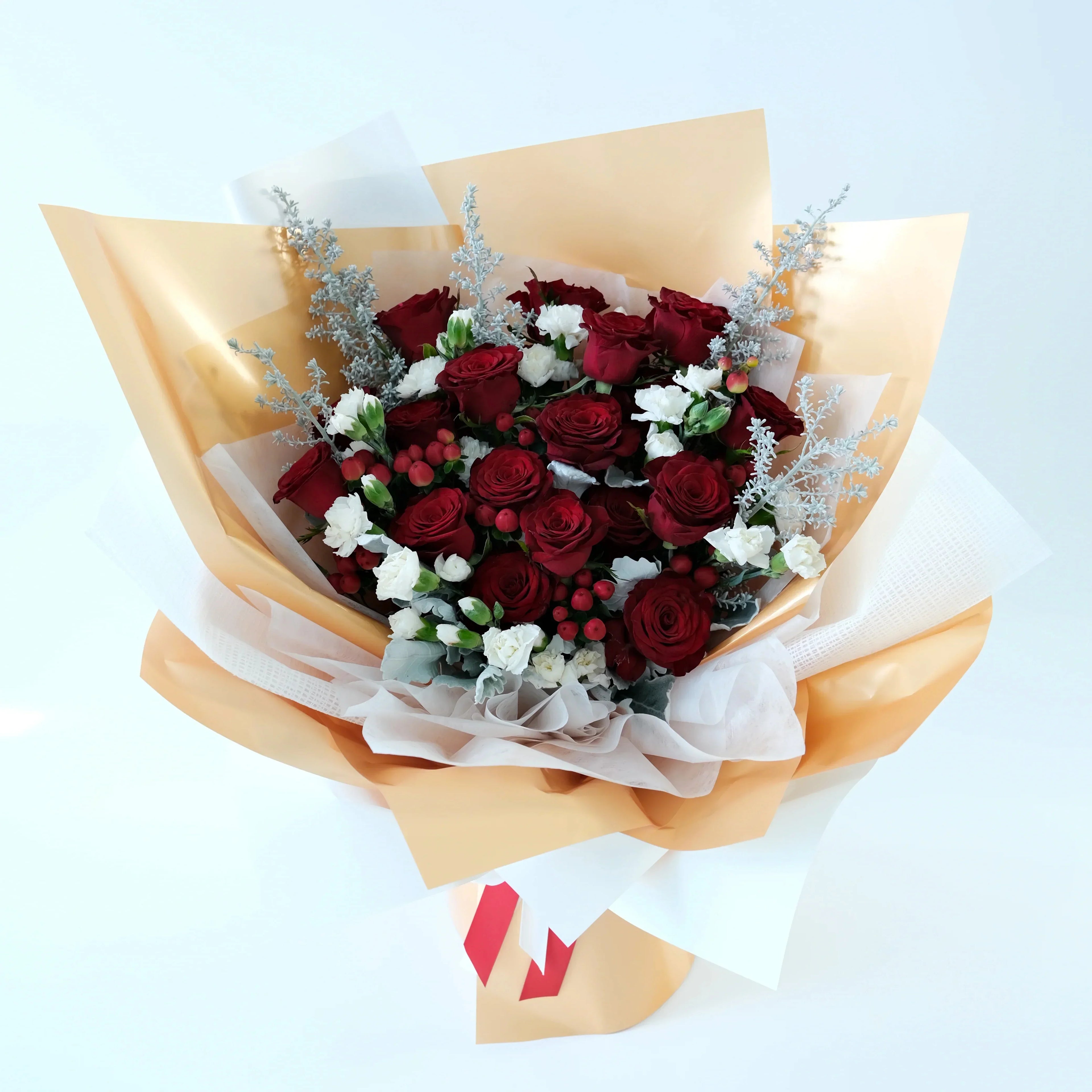 Bouquet of red roses and white flowers wrapped in gold paper on a light blue background