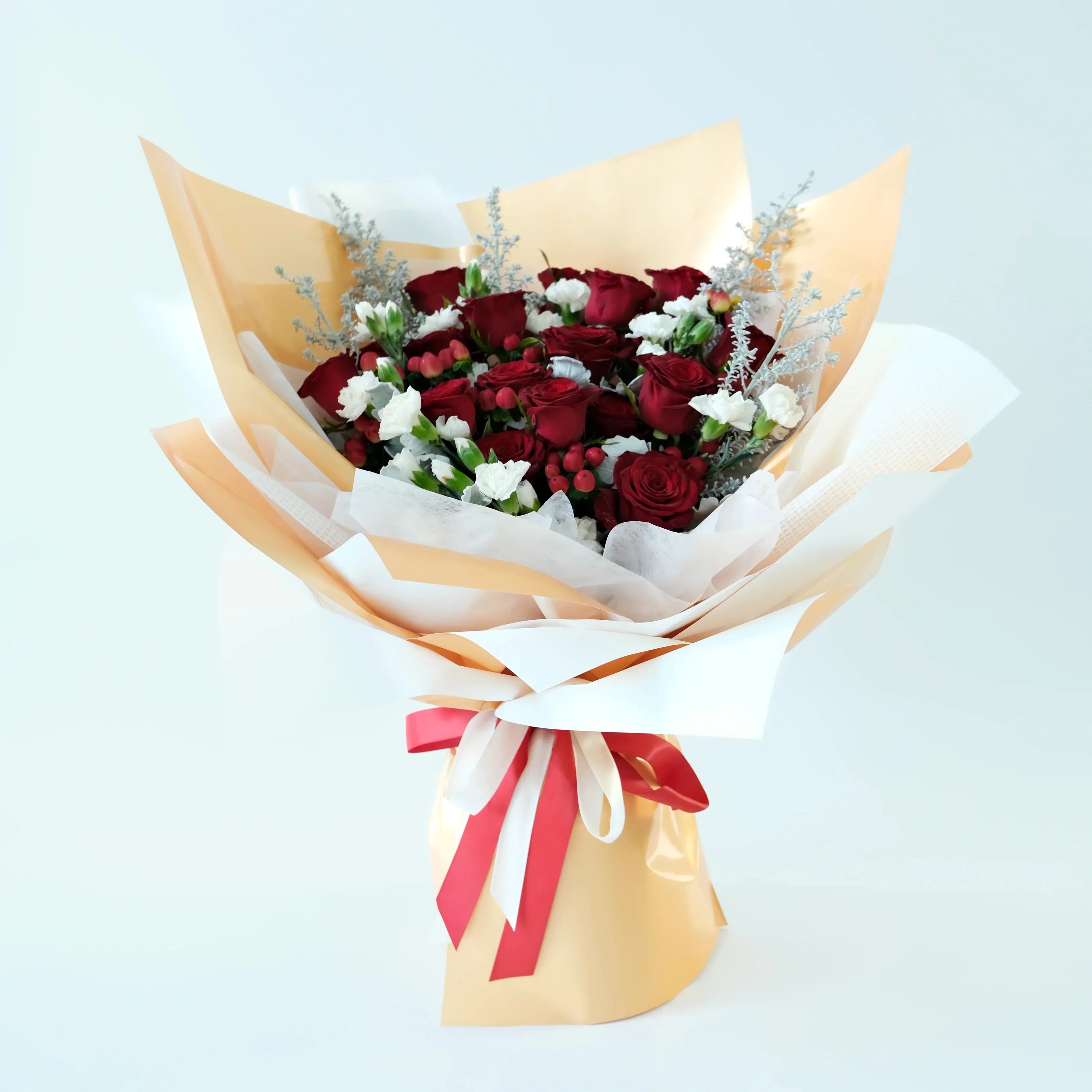 Bouquet of red roses with white accents wrapped in gold paper and a red ribbon on a light blue background