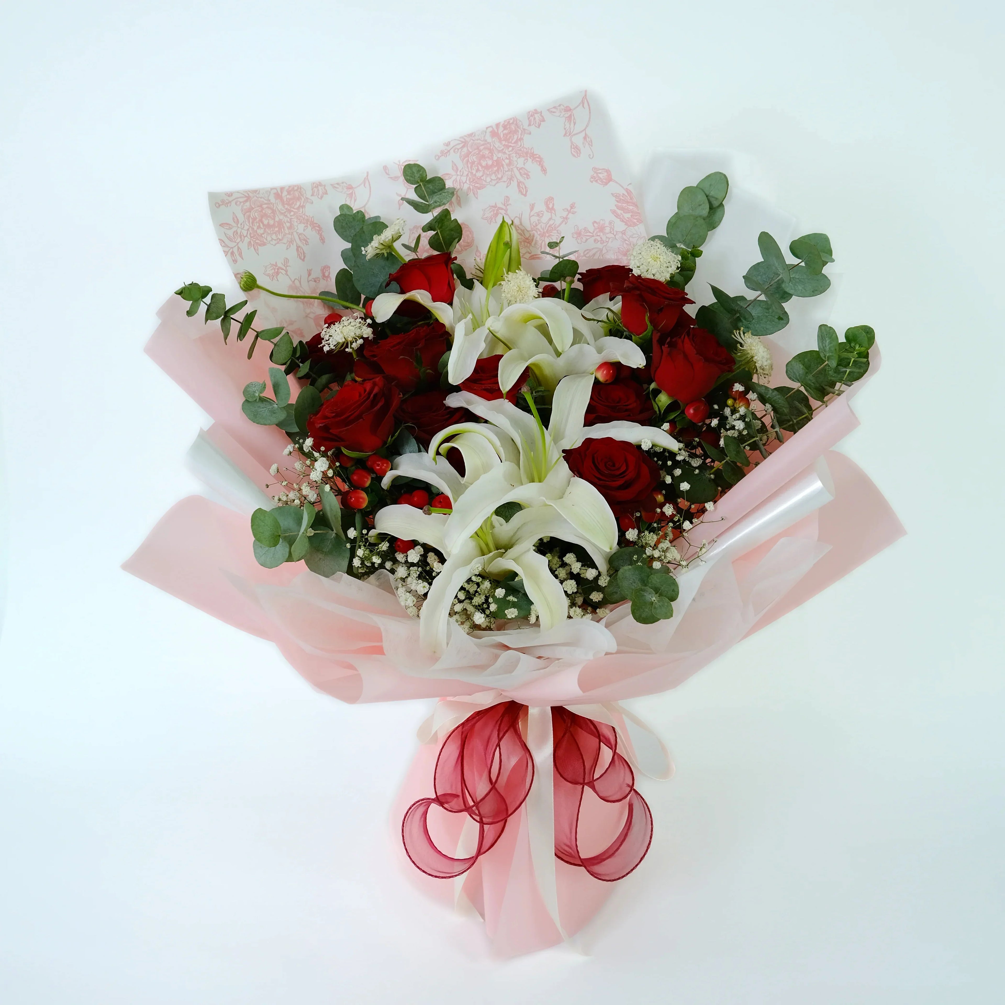 Elegant bouquet with red roses, white lilies, eucalyptus, and pink wrapping for weddings