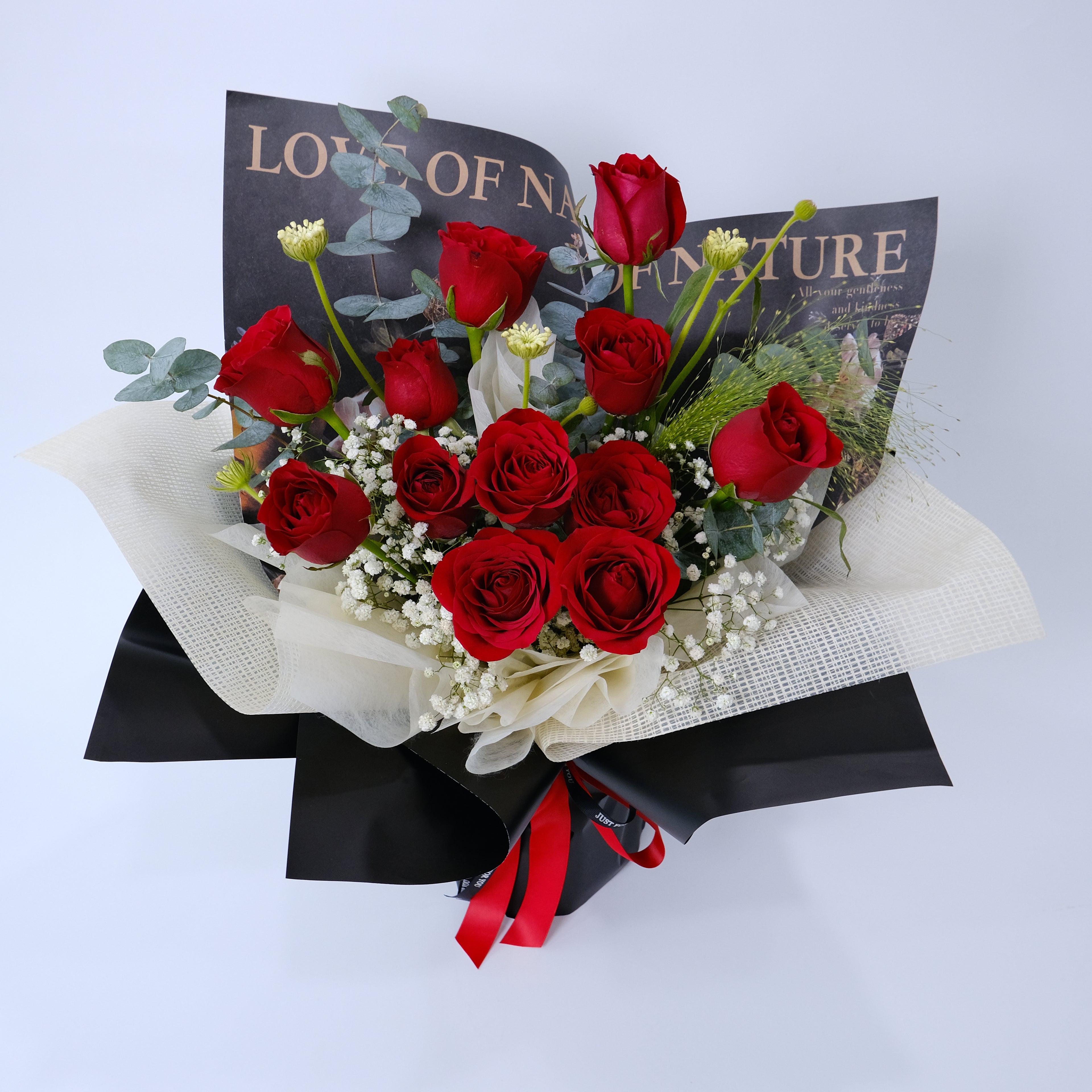 Bouquet of red roses with greenery and a black box on a light blue background