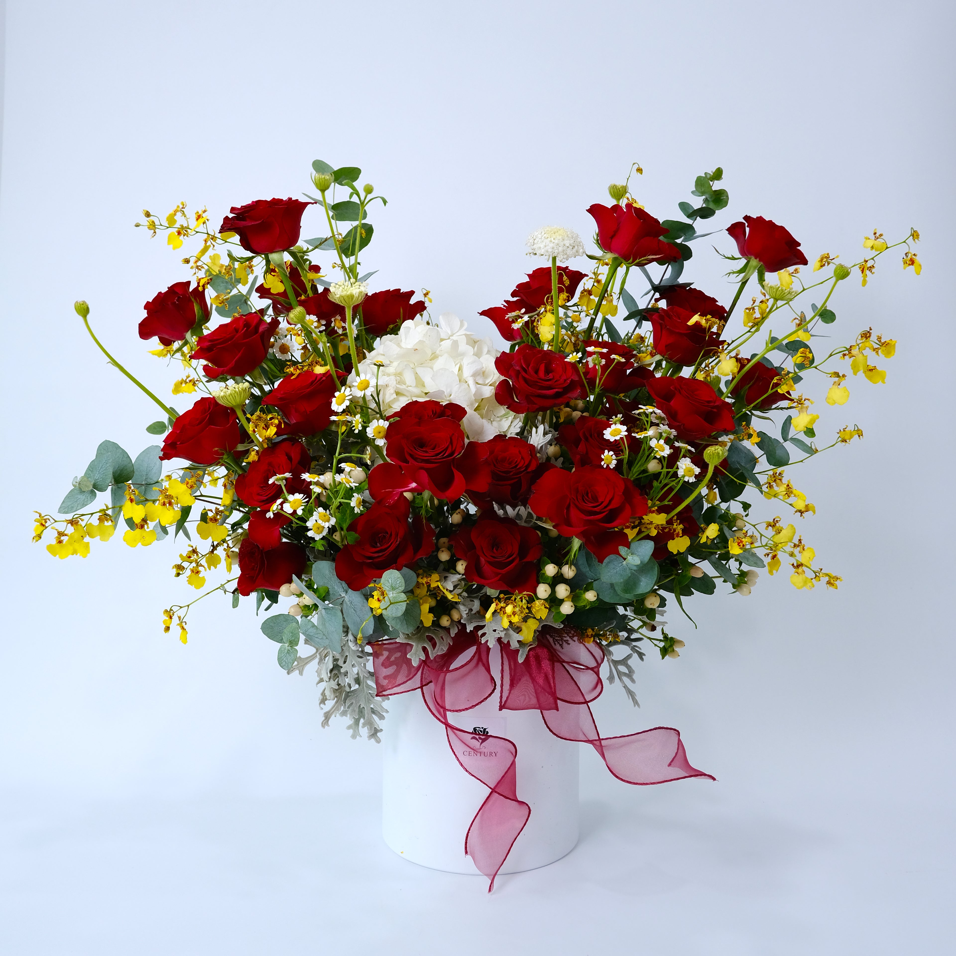 Bouquet of red roses and white flowers with a pink ribbon in a white container on a light gray background