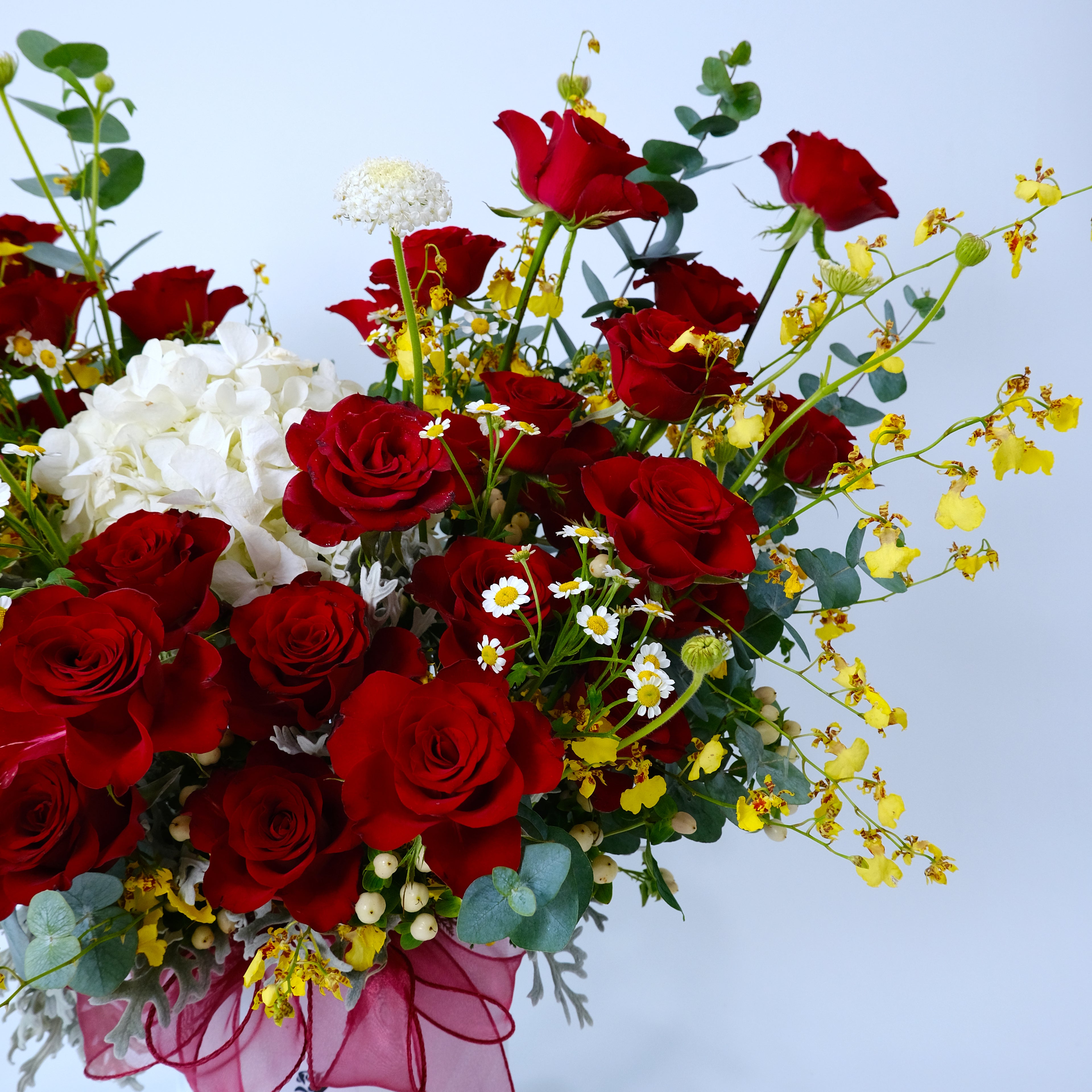 Bouquet of red roses, white flowers, and yellow orchids on a light blue background