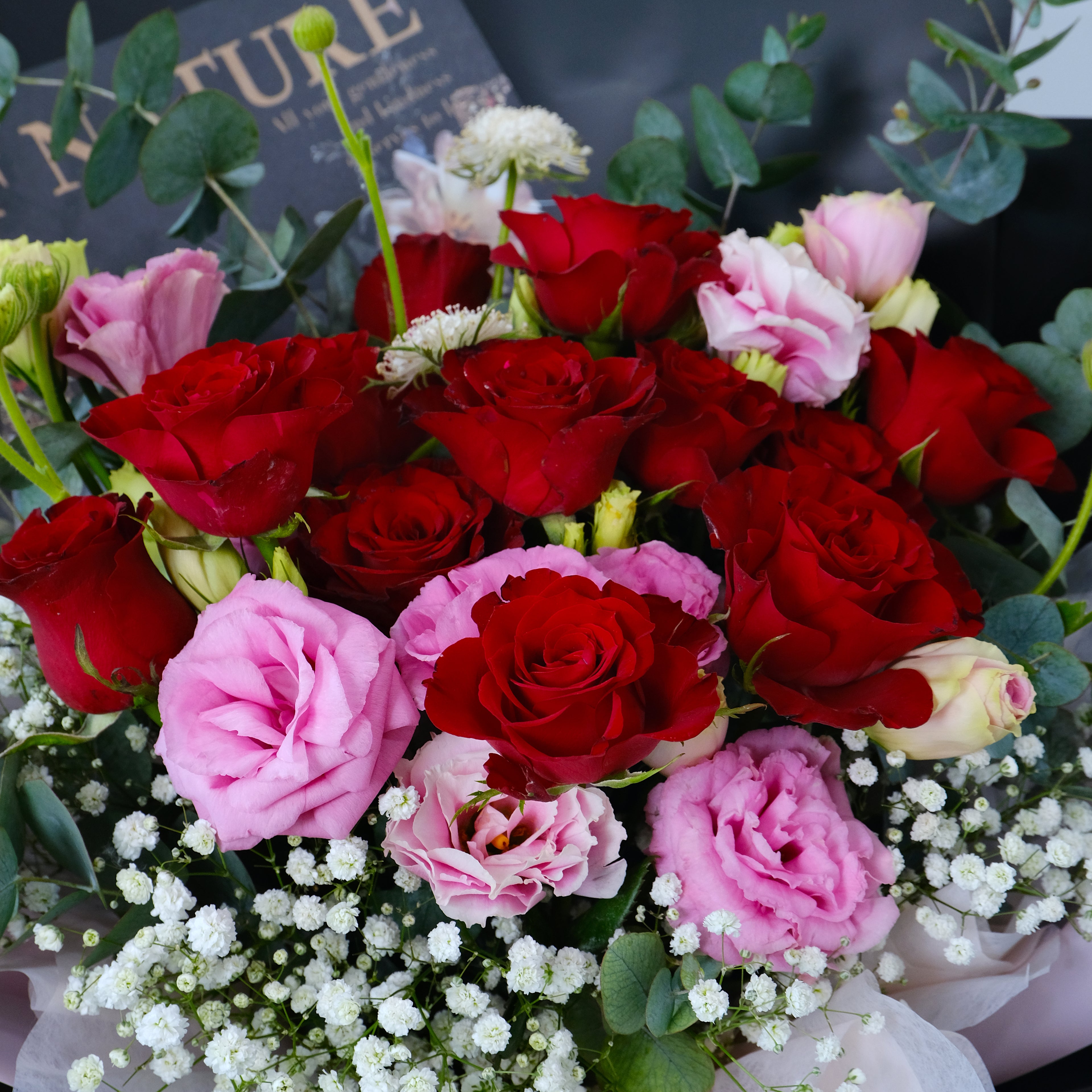 Bouquet of red and pink roses with greenery on a dark background