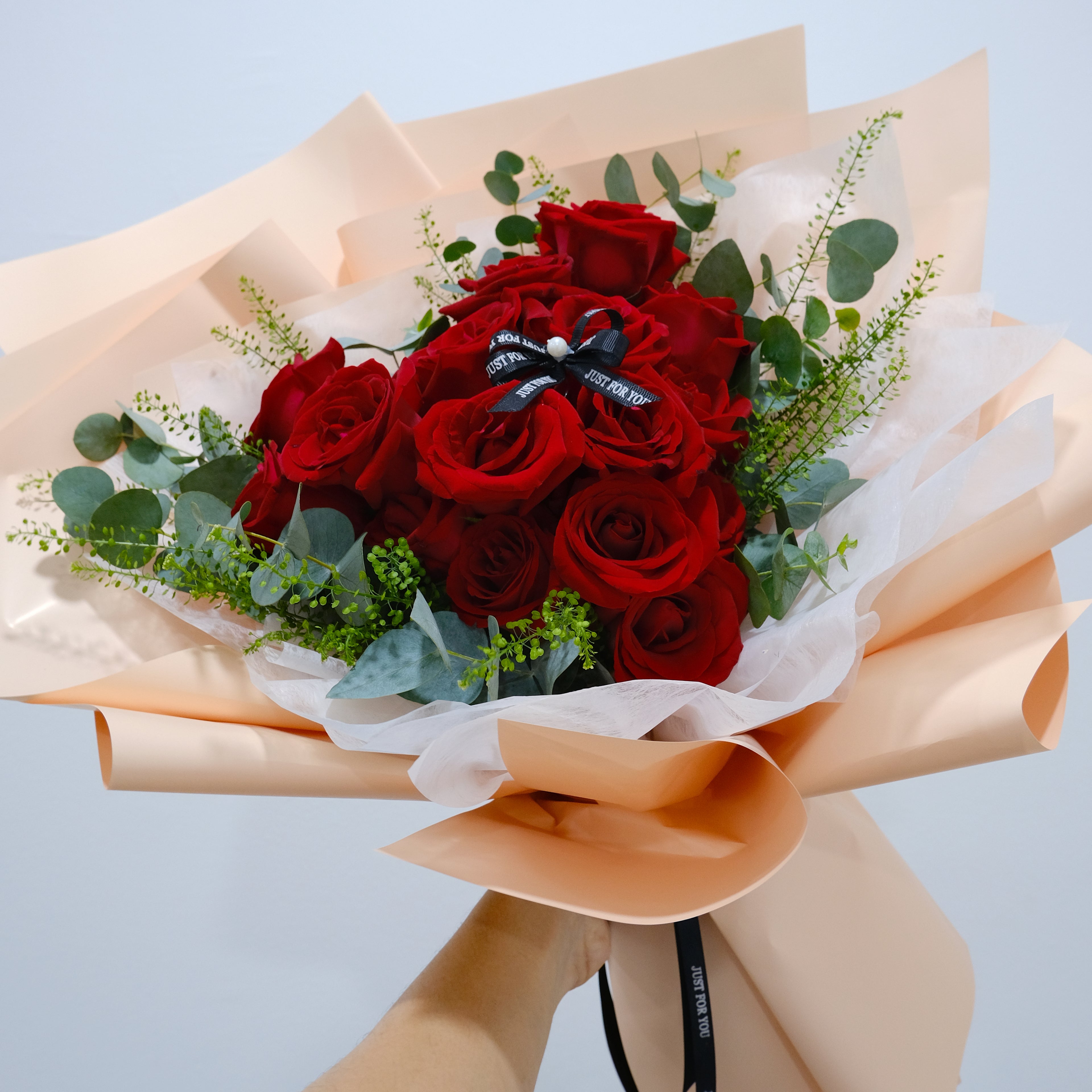 Bouquet of red roses with greenery wrapped in beige paper against a light blue background