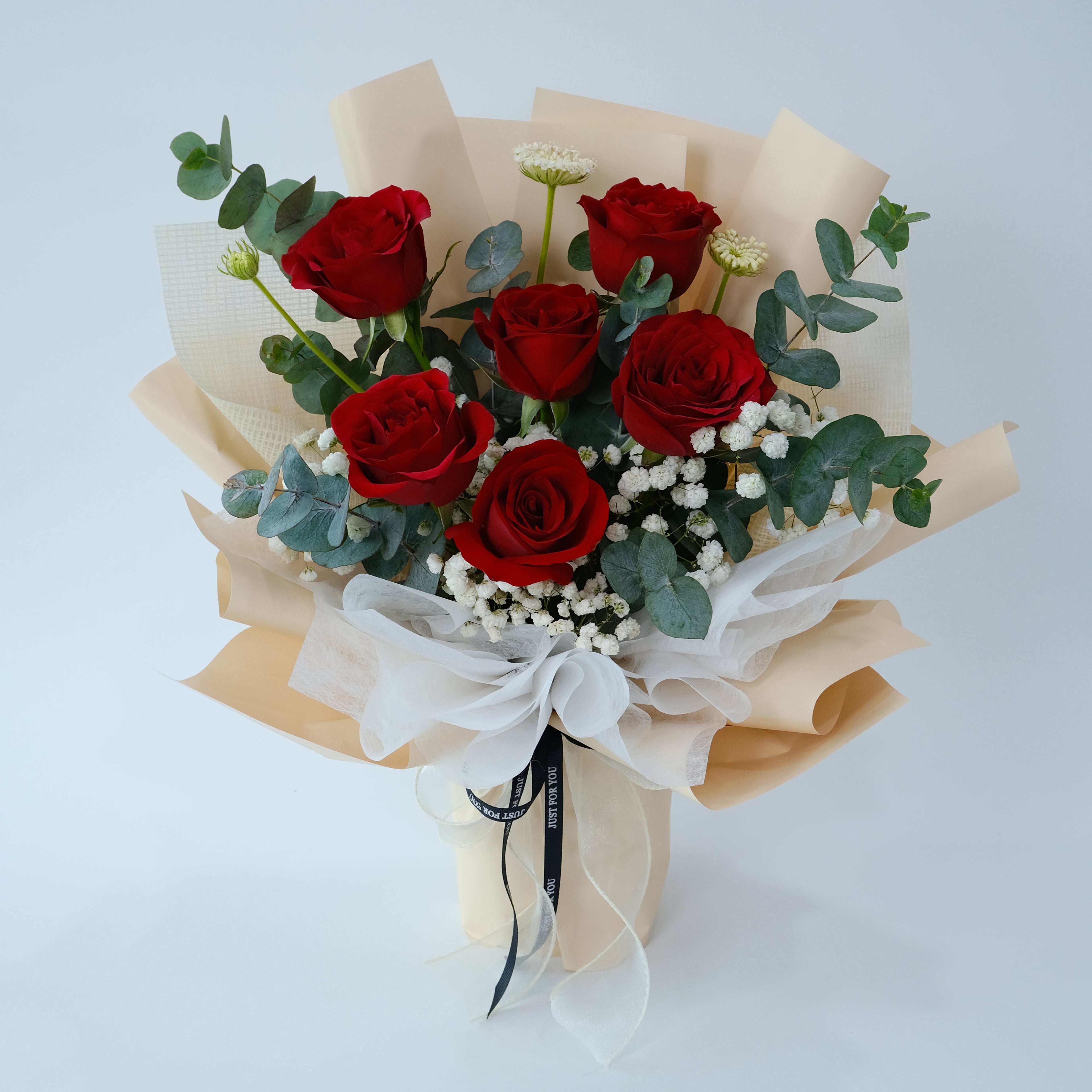 Bouquet of red roses with greenery and a white ribbon on a light blue background