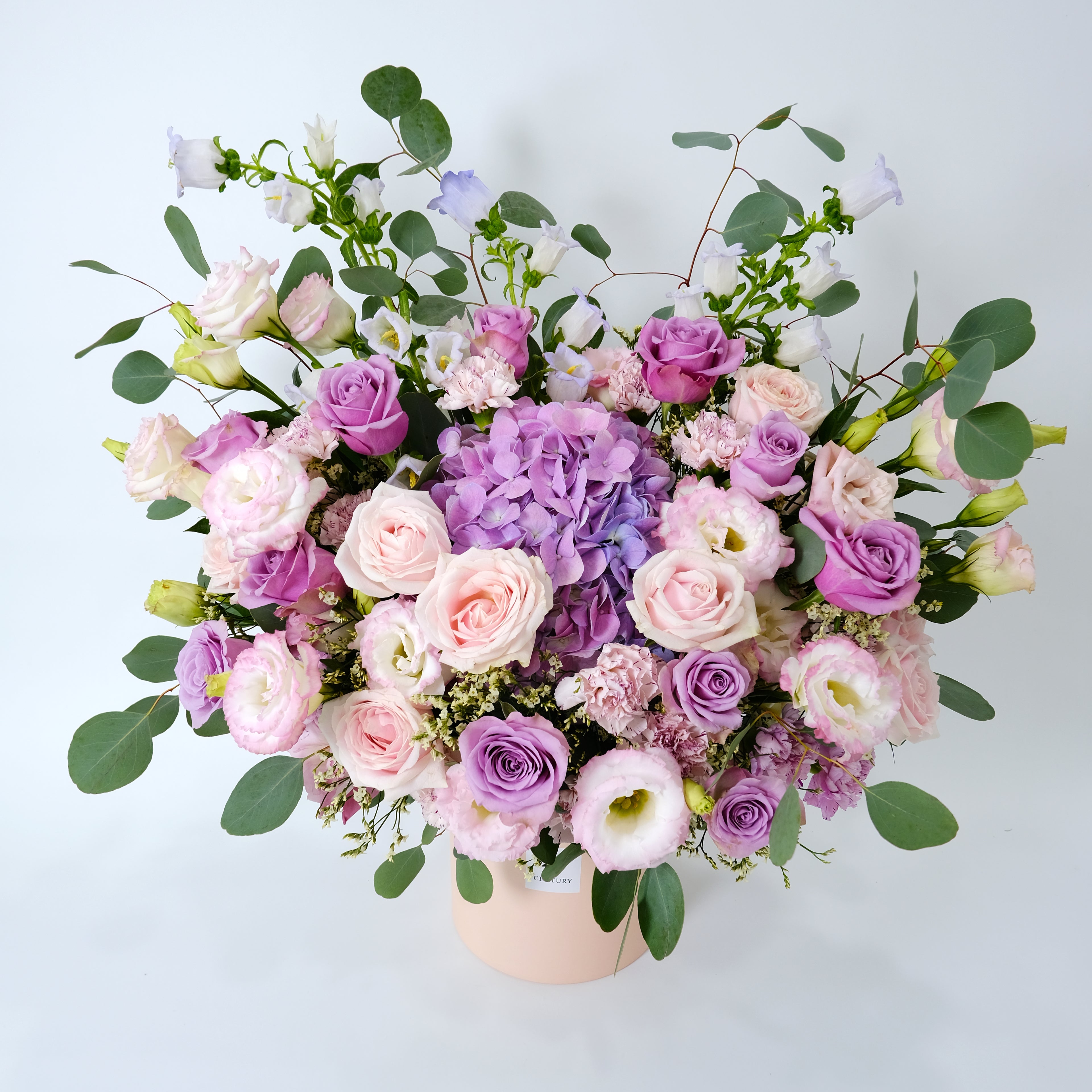Bouquet of pink and purple flowers with green leaves in a white container on a light gray background