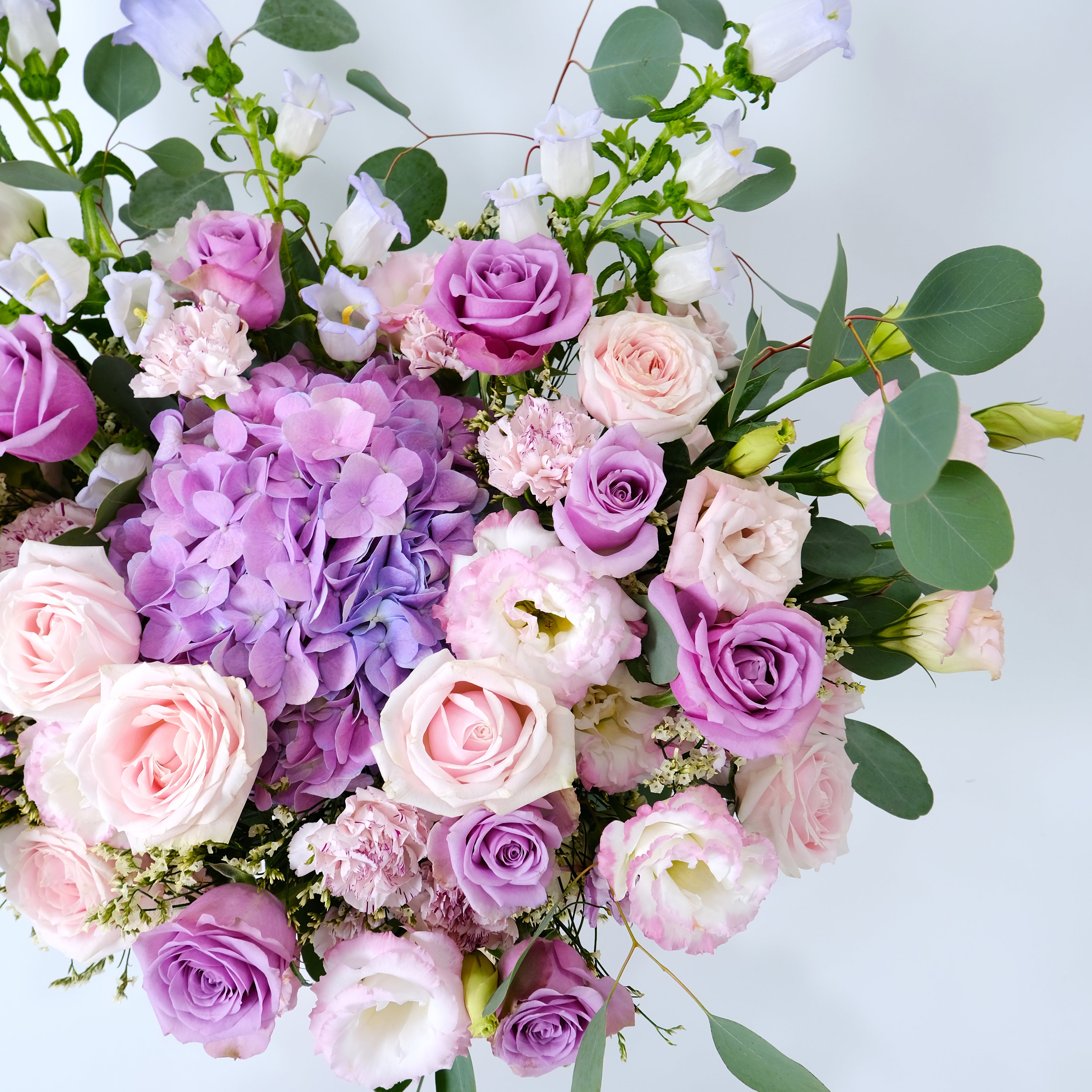 Bouquet of pink, purple, and white flowers with green leaves on a light blue background