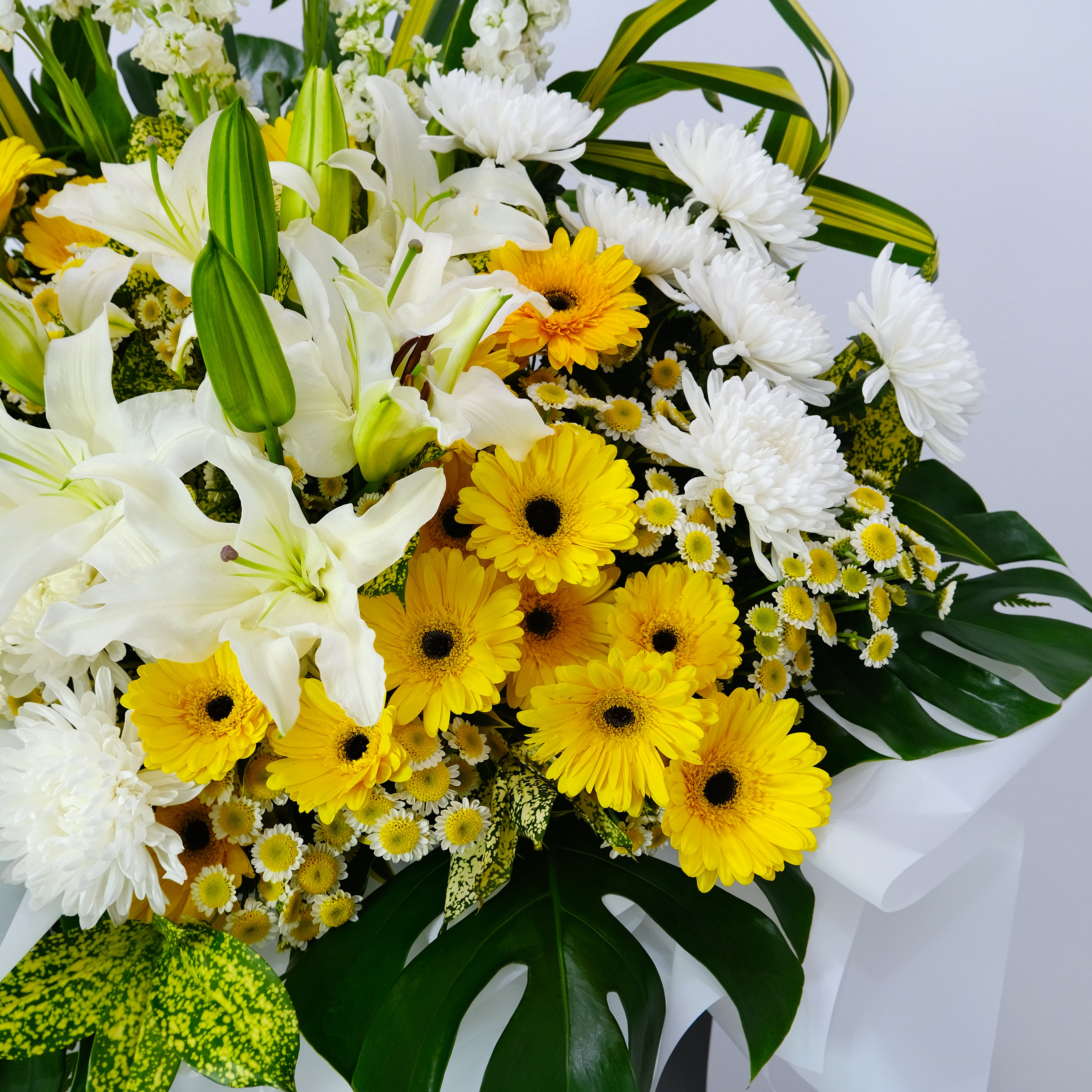 condolence flower stand of yellow and white flowers with green leaves on a light gray background