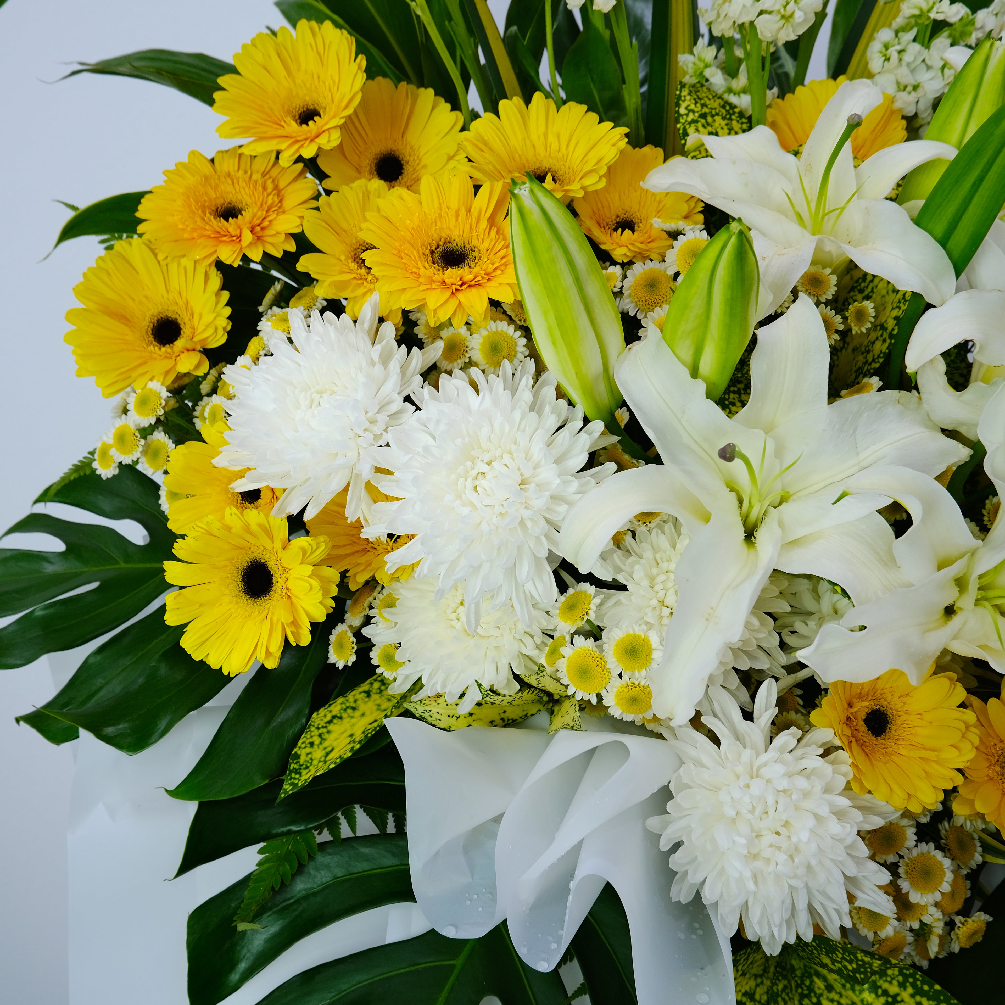 condolence flower stand of yellow and white flowers with green leaves on a light gray background