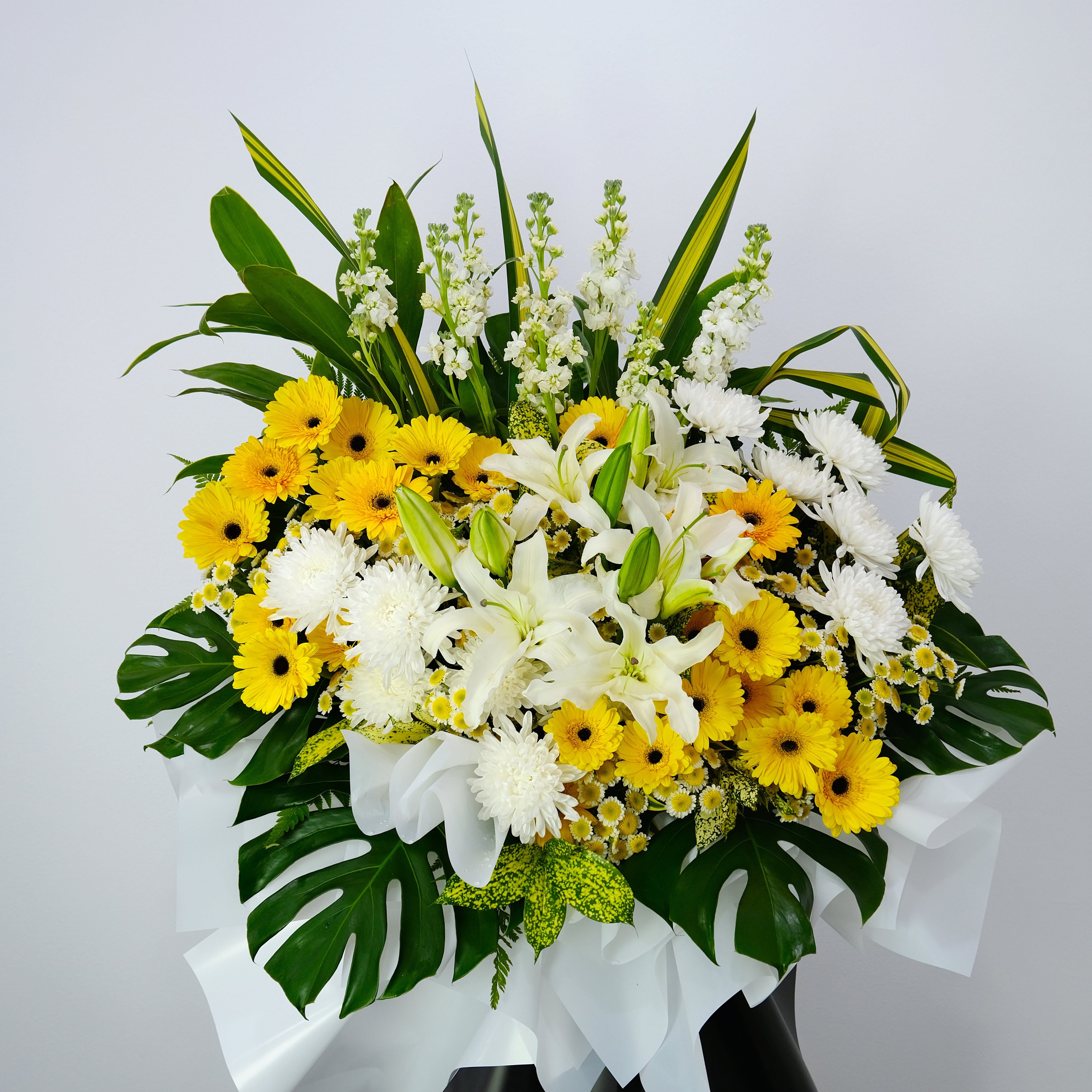 condolence flower stand of yellow and white flowers with green leaves on a light gray background