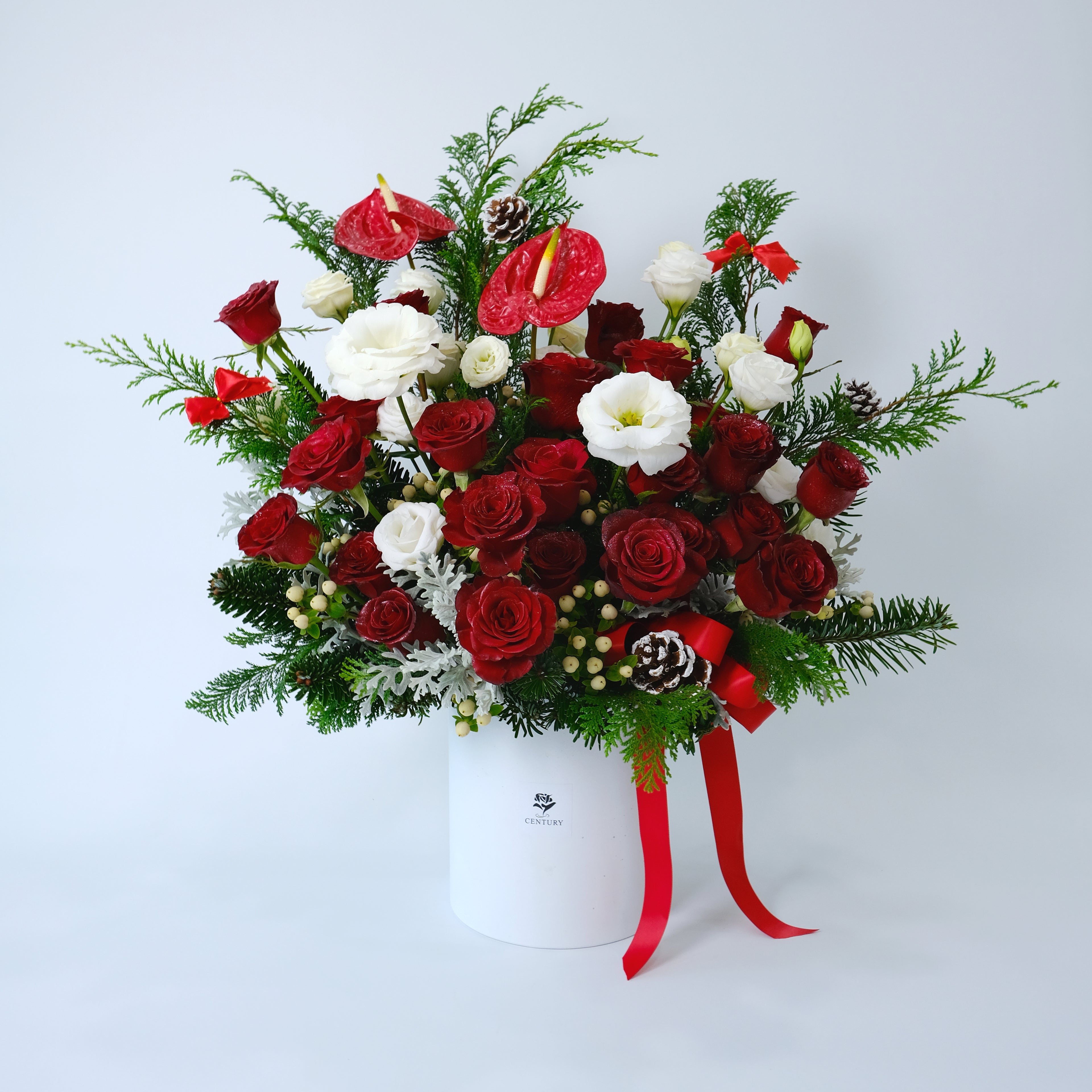 Bouquet of red and white flowers with greenery in a white box on a light gray background