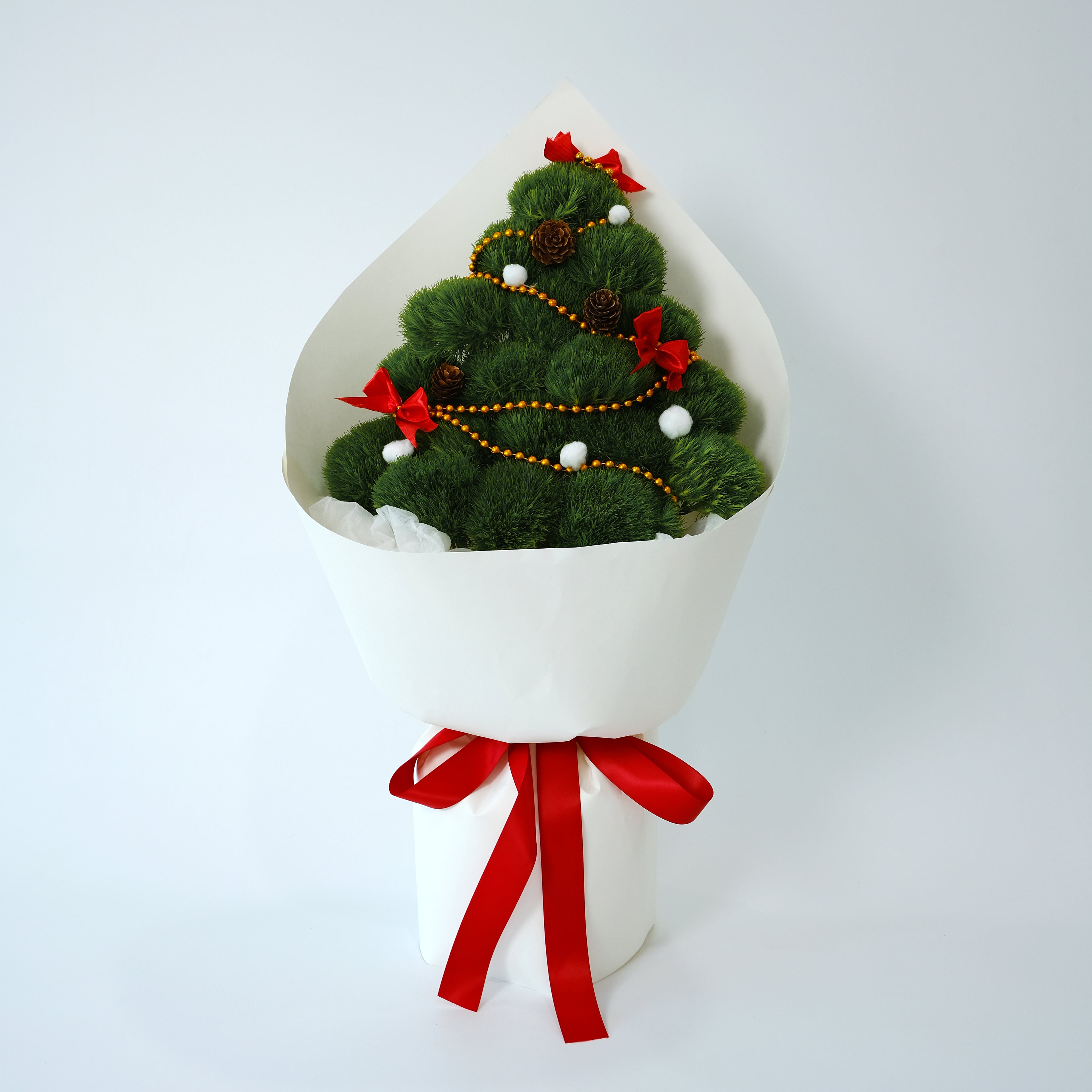 Decorative Christmas tree in a white box with red ribbons on a light gray background
