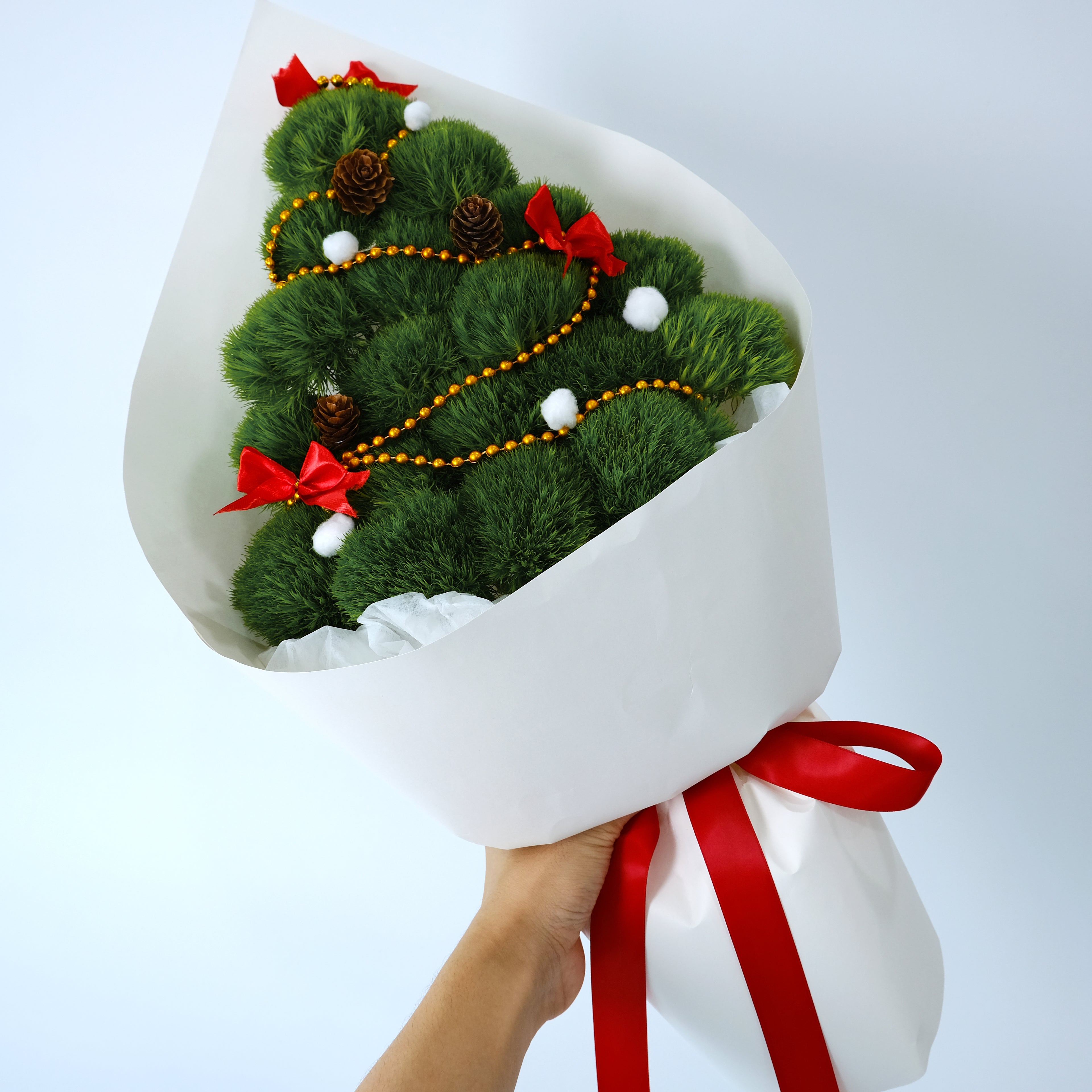 Bouquet shaped like a Christmas tree with decorative ribbons and pinecones on a white background
