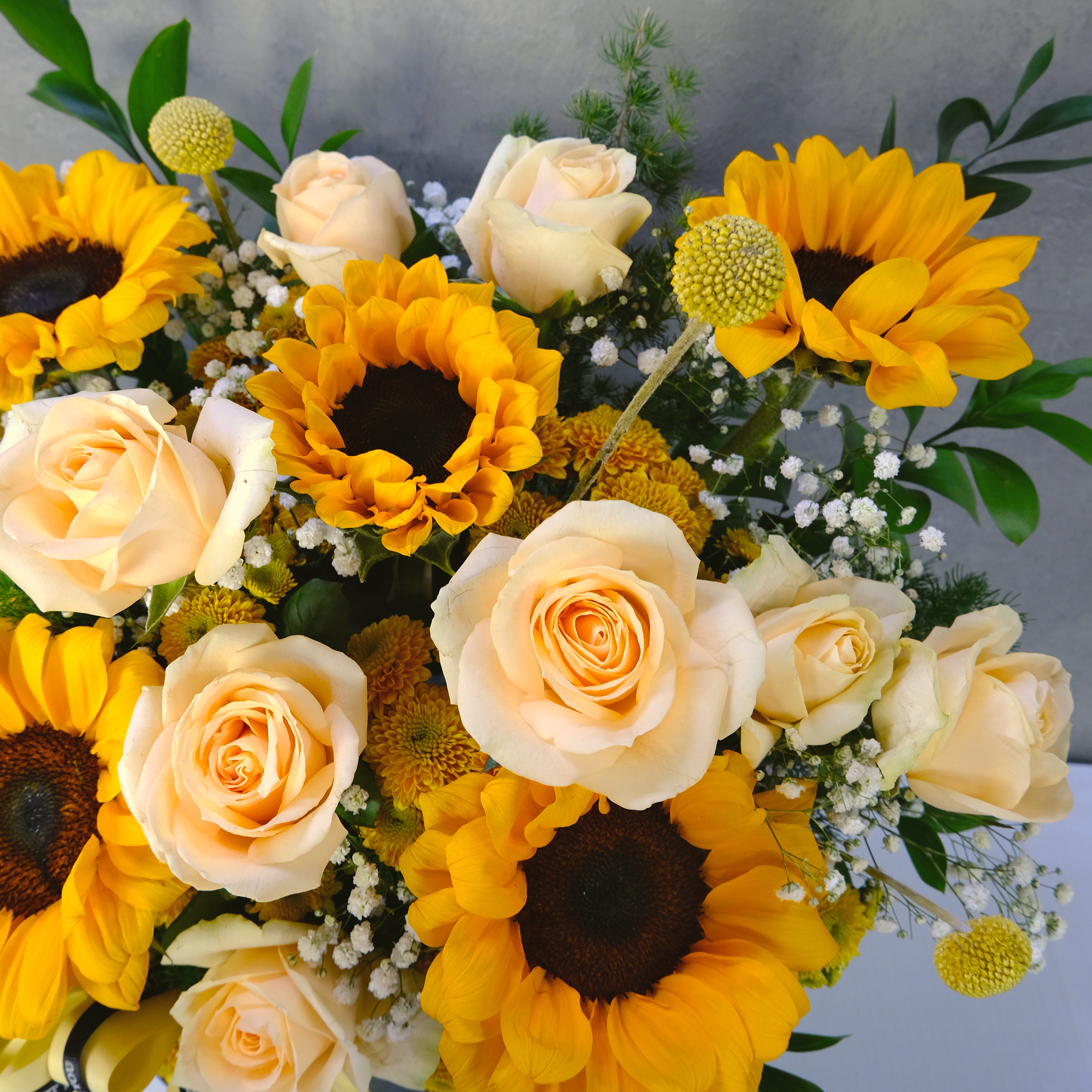 Bouquet of yellow sunflowers and white roses with greenery on a light gray background