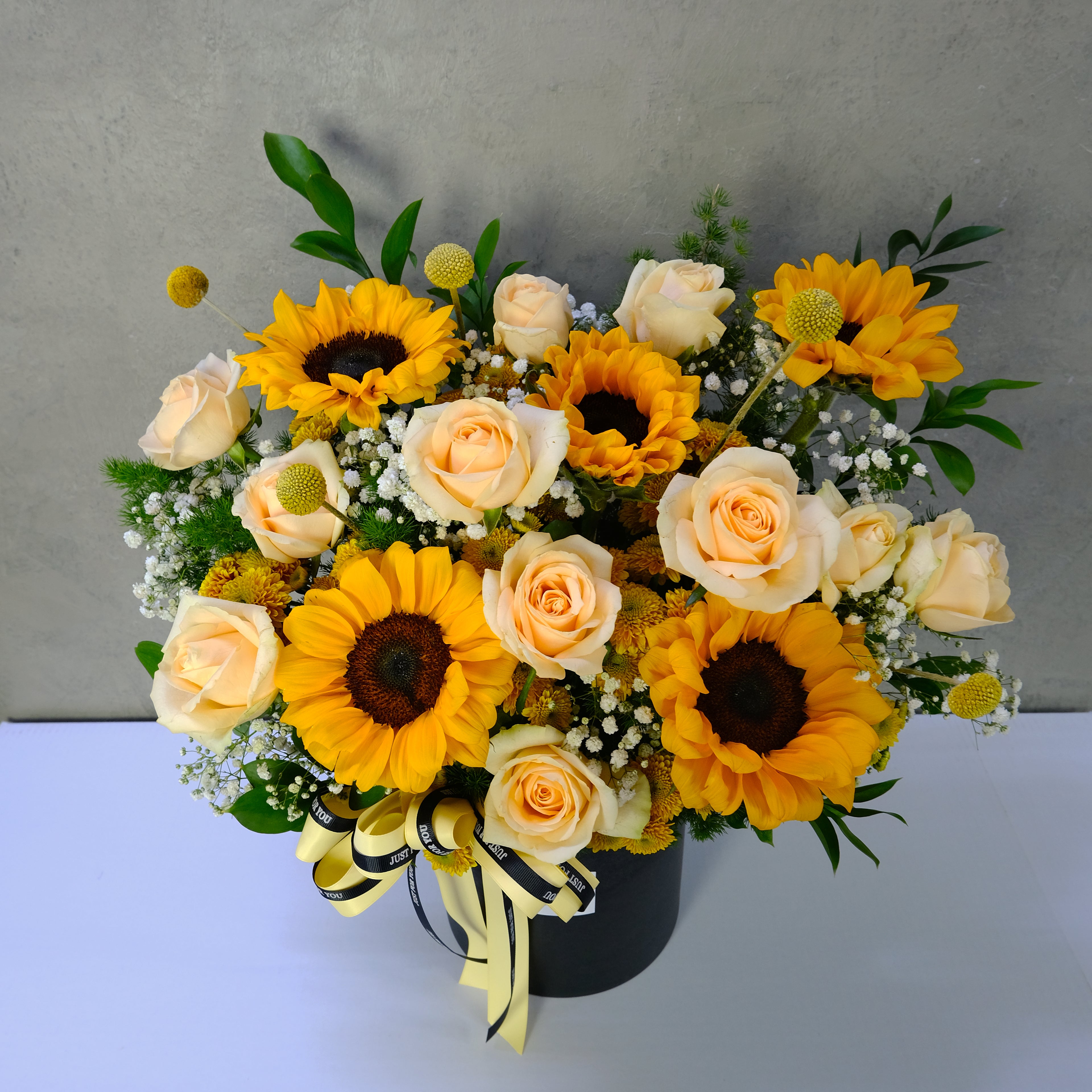 Bouquet of yellow sunflowers and white roses with a black container on a light gray background
