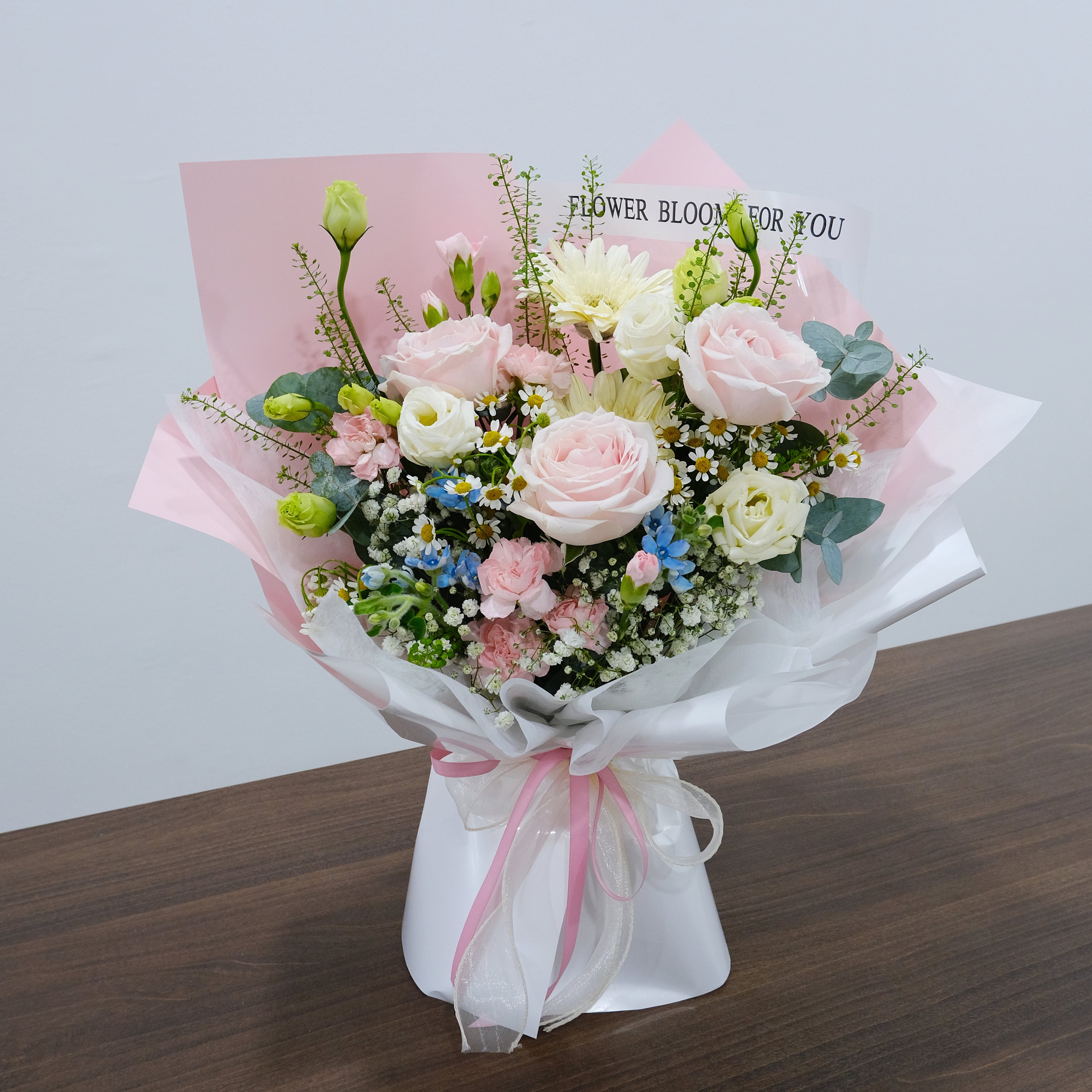 Bouquet of flowers with pink and white ribbons on a wooden surface