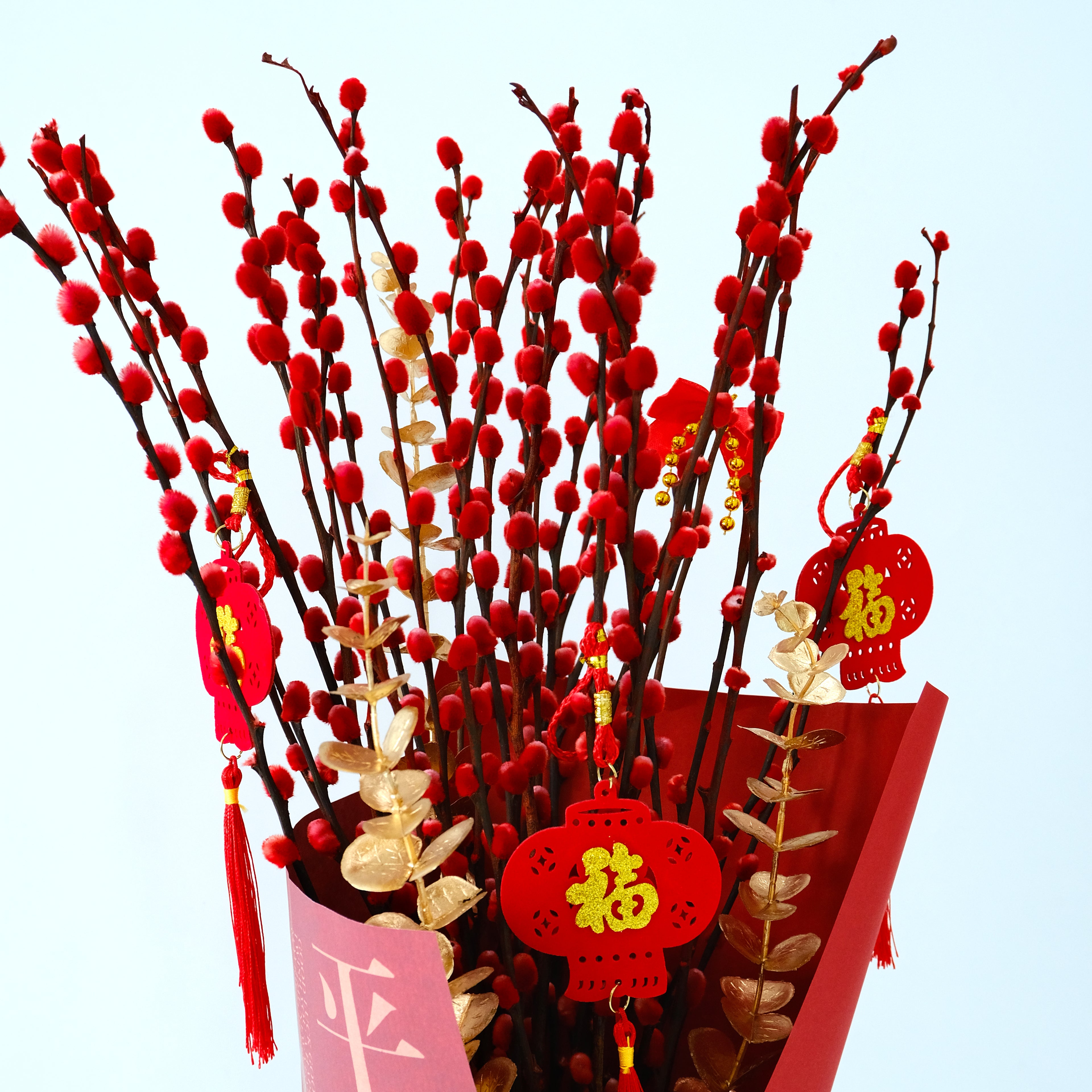 Decorative arrangement of red and gold plants with festive decorations on a light blue background