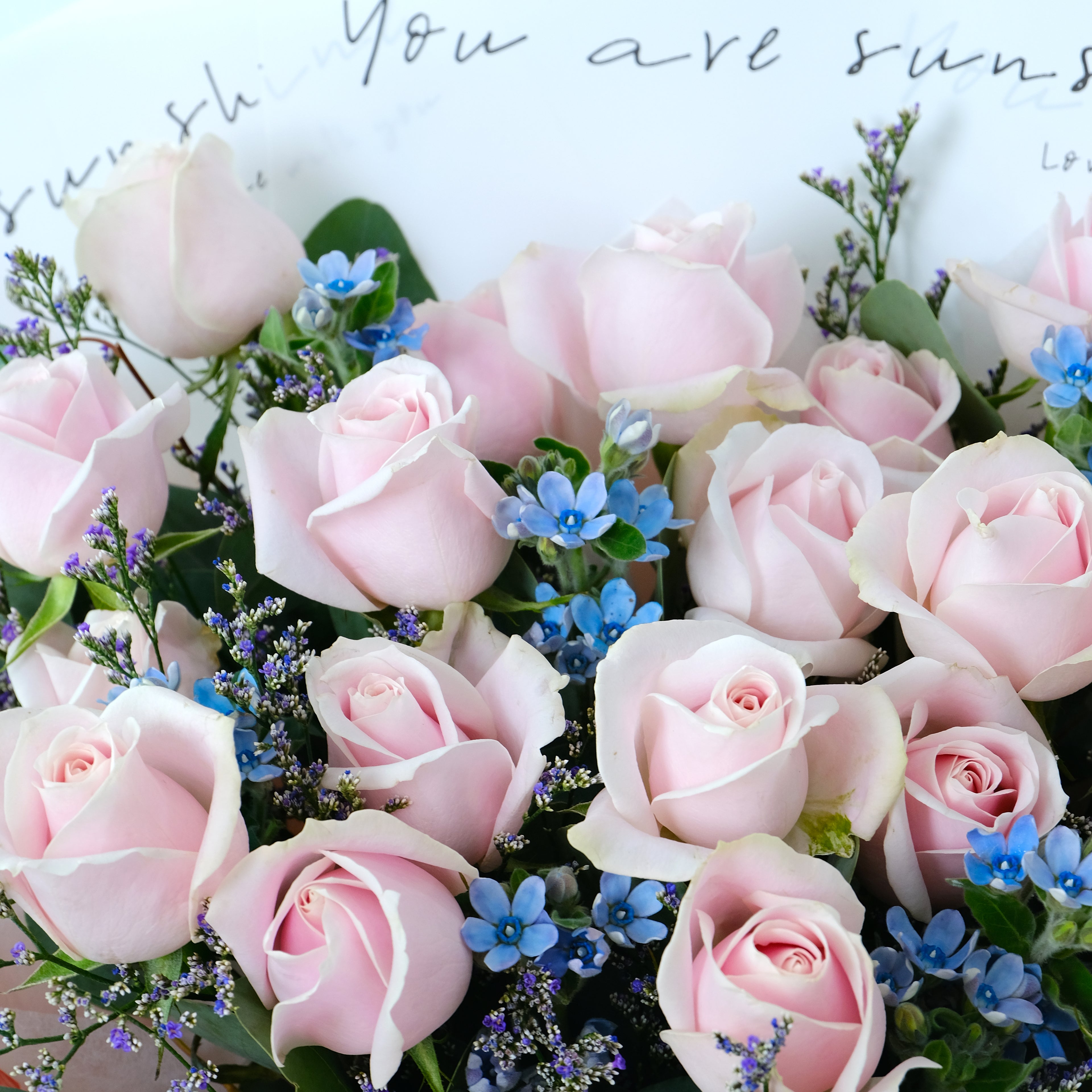 Bouquet of pink roses with greenery and small blue flowers on a light background.