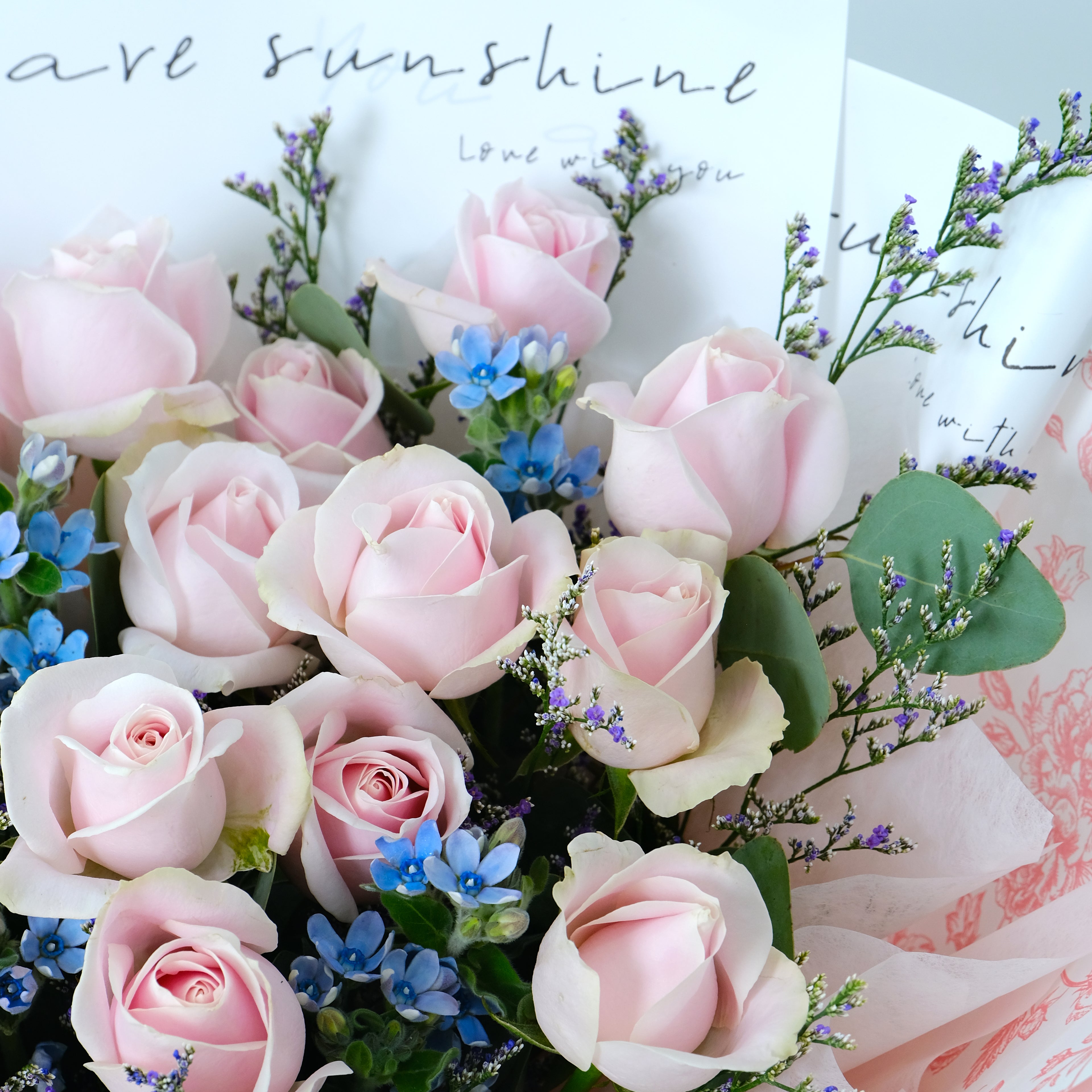 Bouquet of pink roses with green leaves and small blue flowers on a white background.
