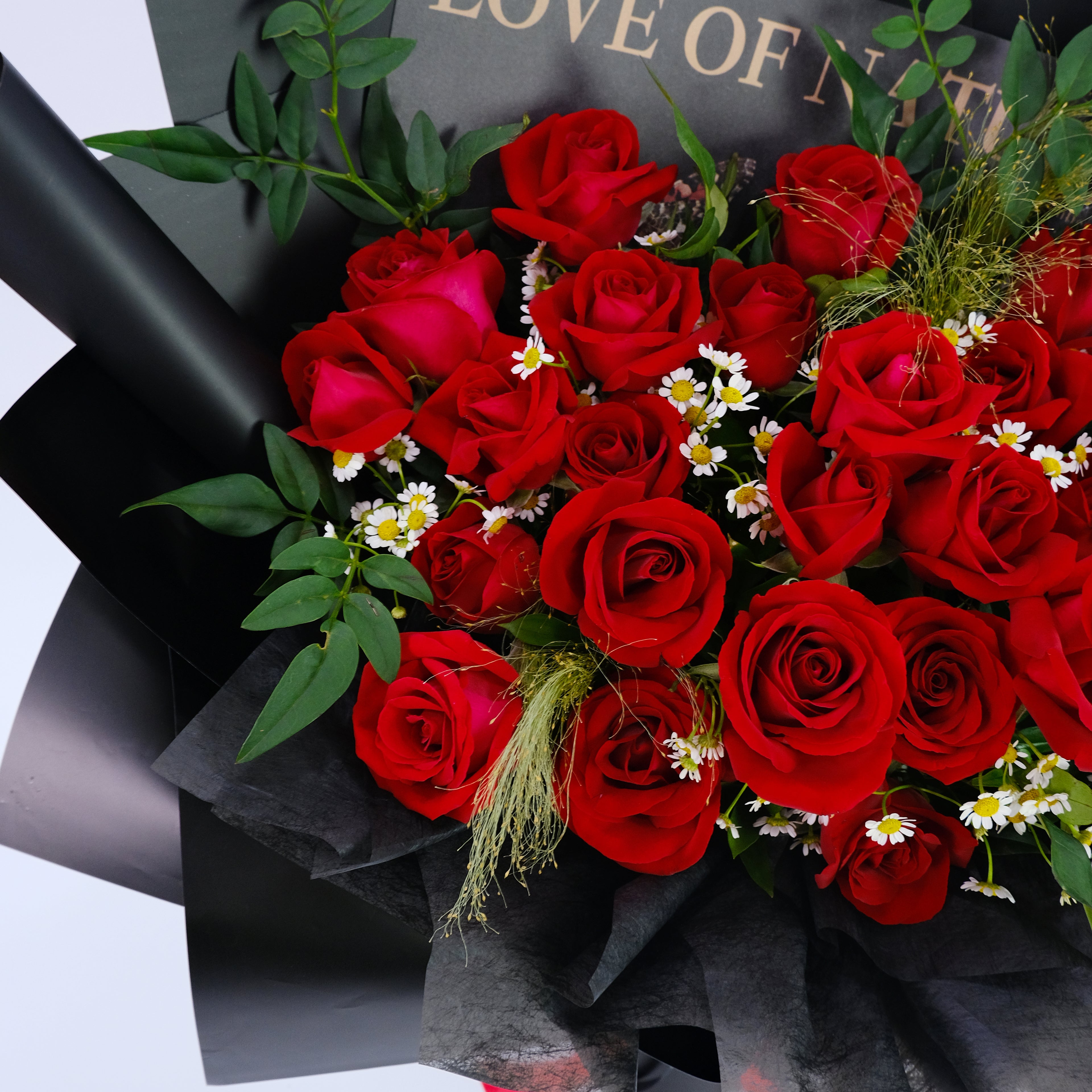 Bouquet of red roses with greenery on a black wrap, with 'LOVE OF' text in the background.