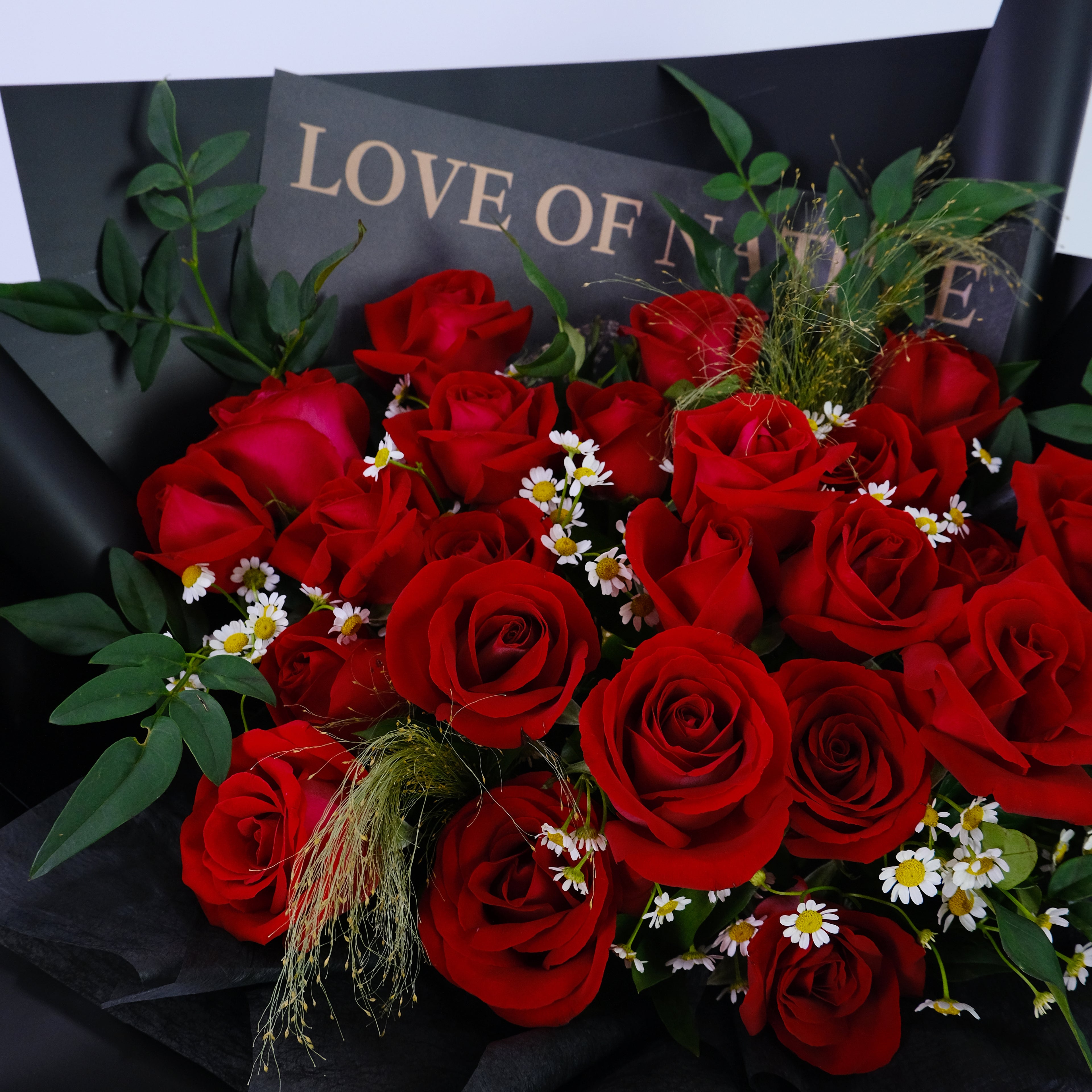 Bouquet of red roses with green leaves and small white flowers on a black background with 'LOVE OF' text.