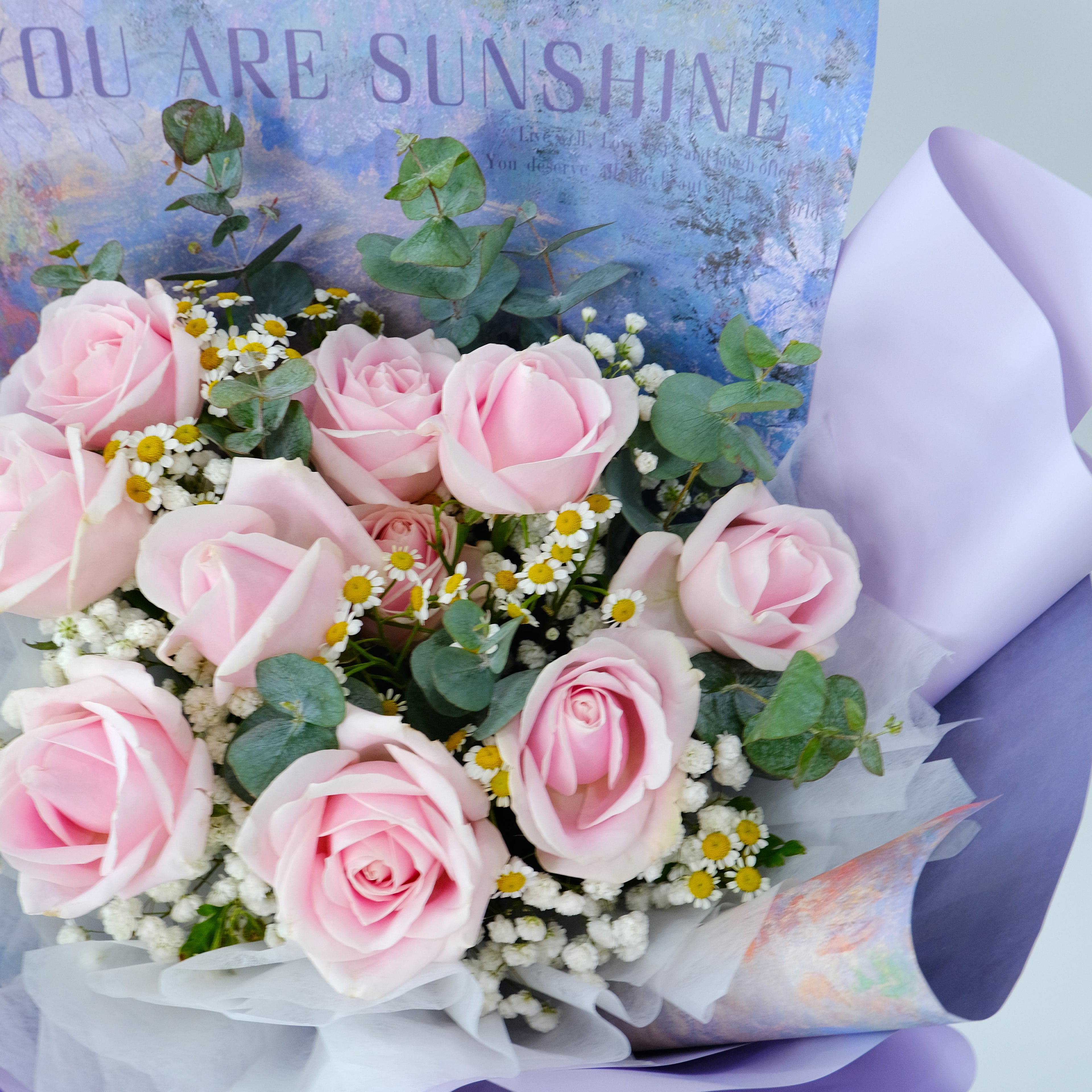 Bouquet of pink roses with greenery and a card saying 'You are sunshine' in the background.