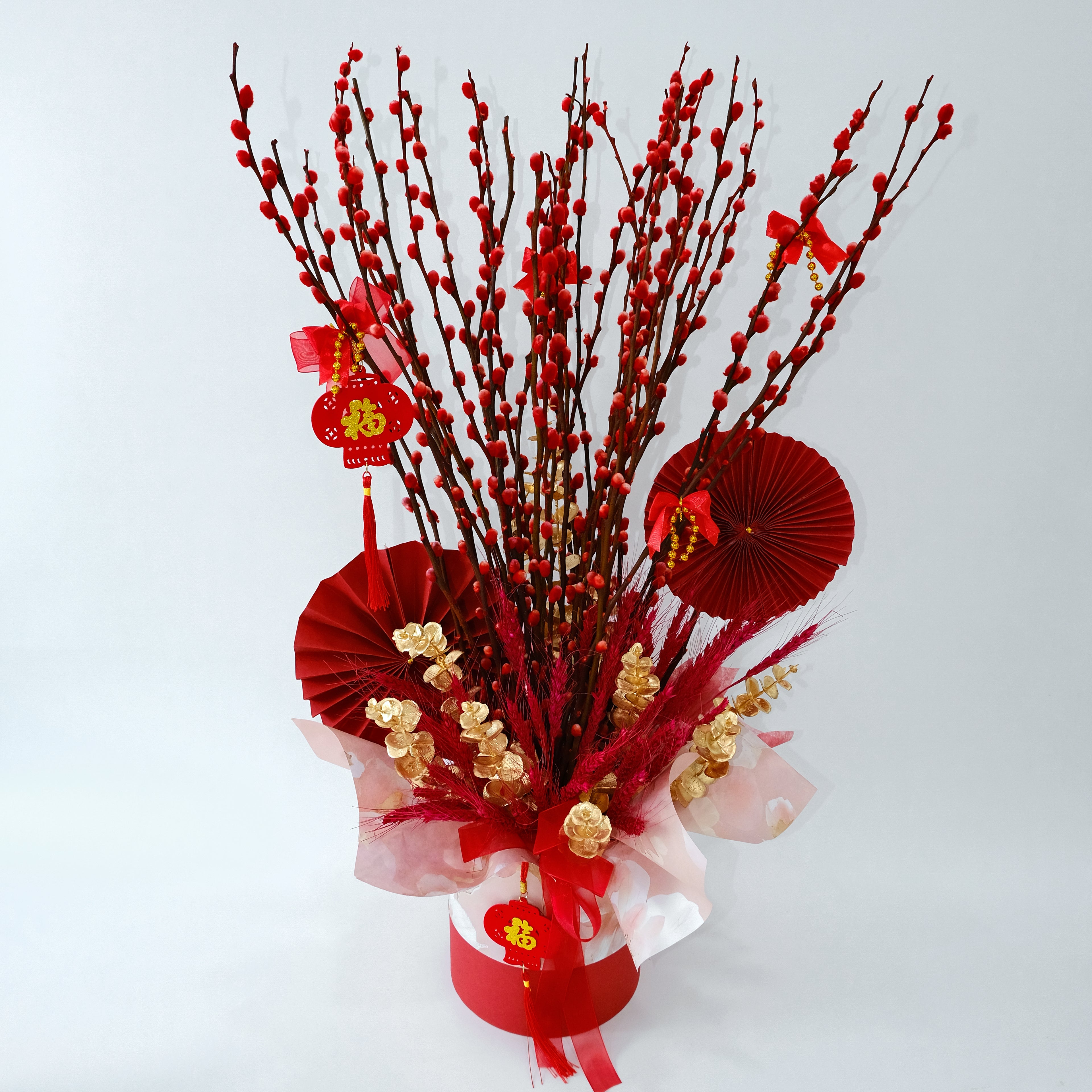 Decorative arrangement with red pussy willow branches, paper fans, and ribbons on a white background