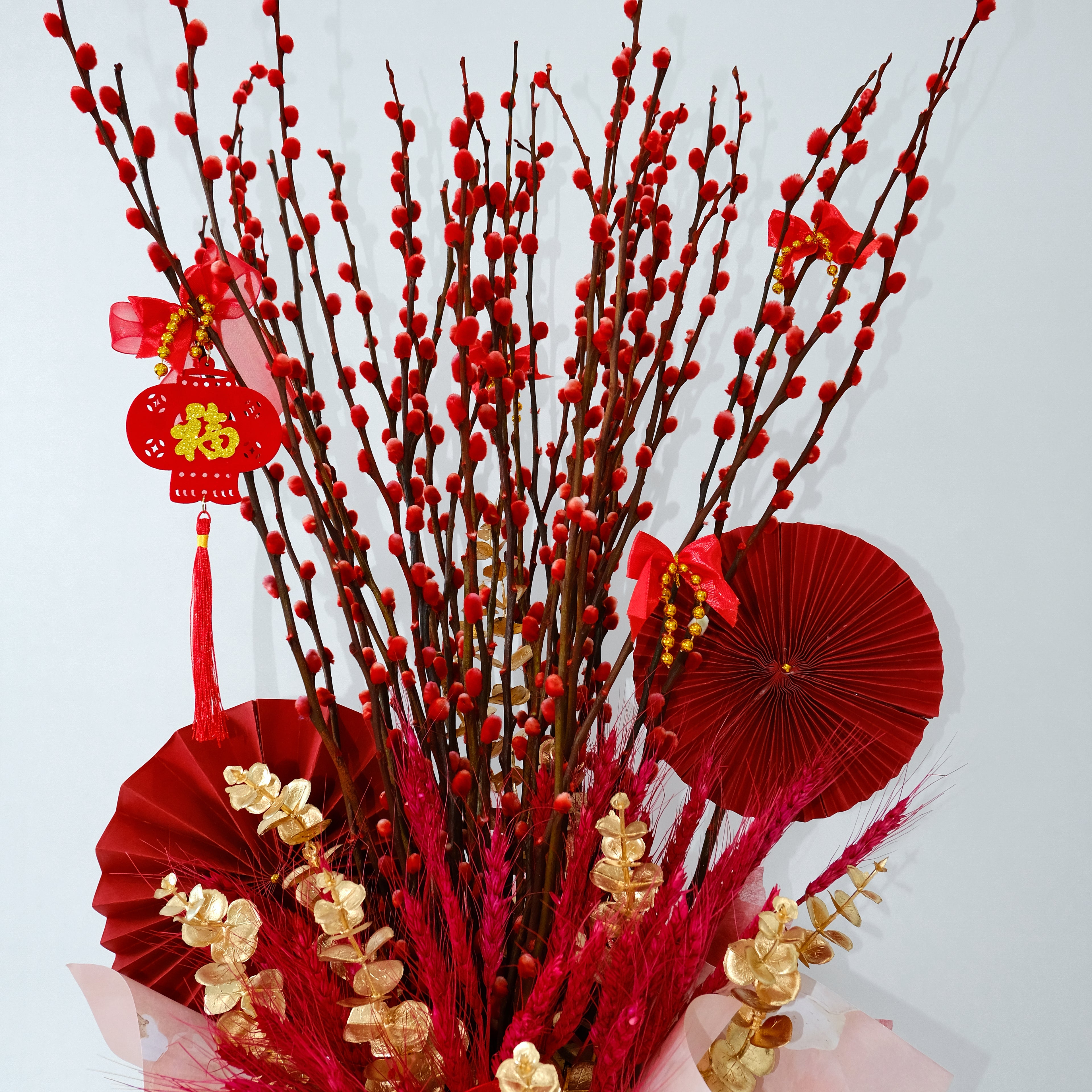 Decorative arrangement with red pussy willow flowers, red paper fans, and gold elements on a white background