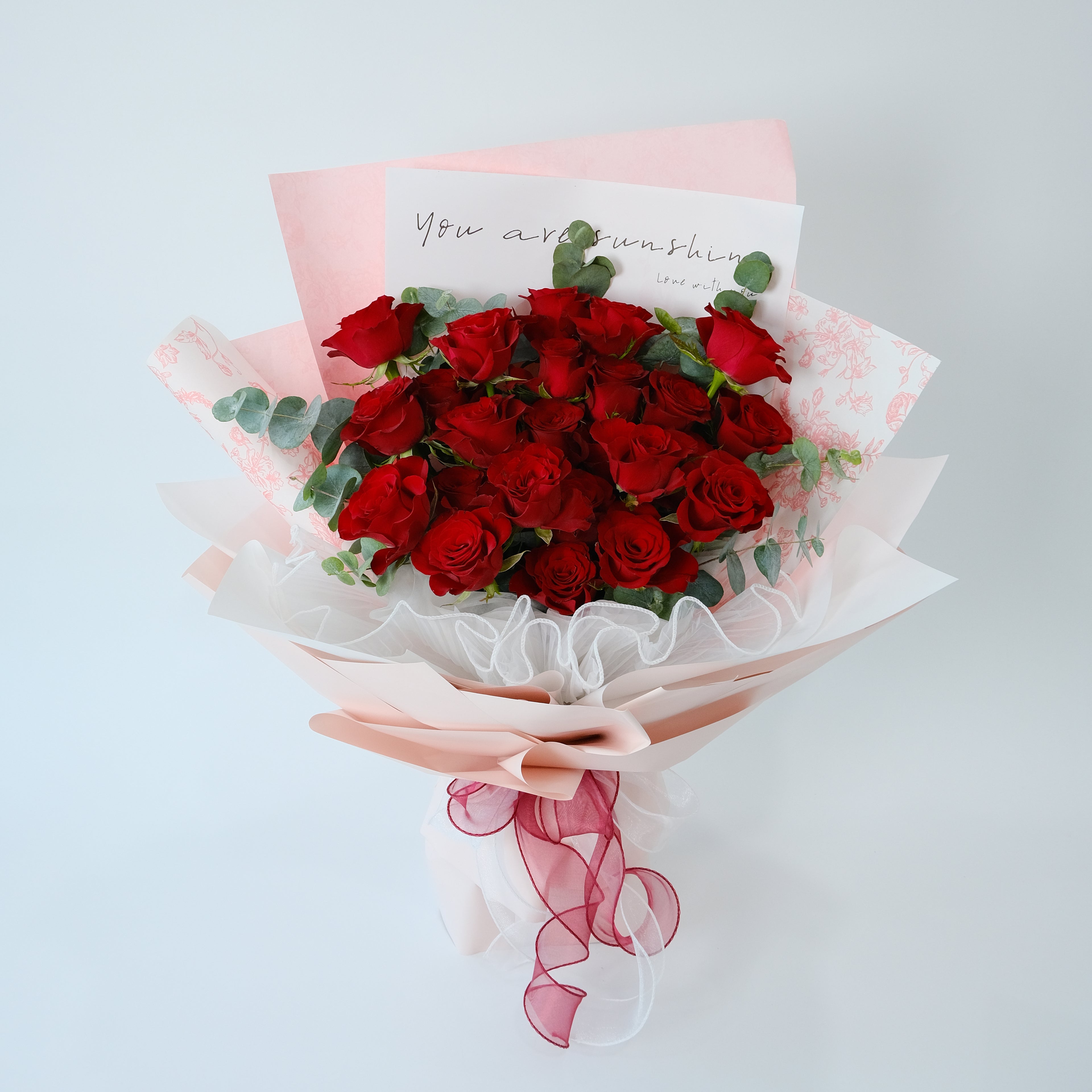 Bouquet of red roses with a pink ribbon and a card on a light gray background