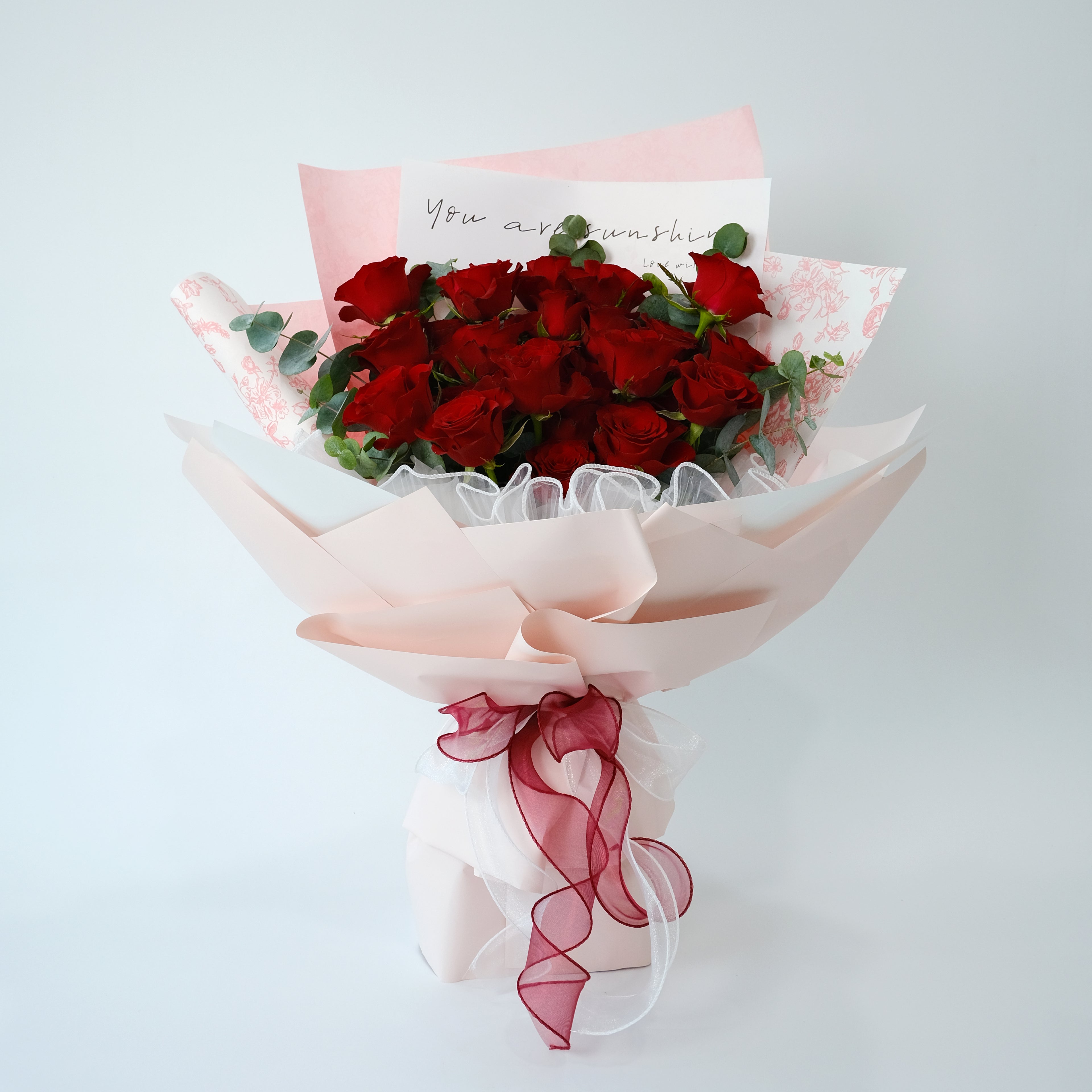 Bouquet of red roses wrapped in pink paper with a red ribbon on a light gray background.