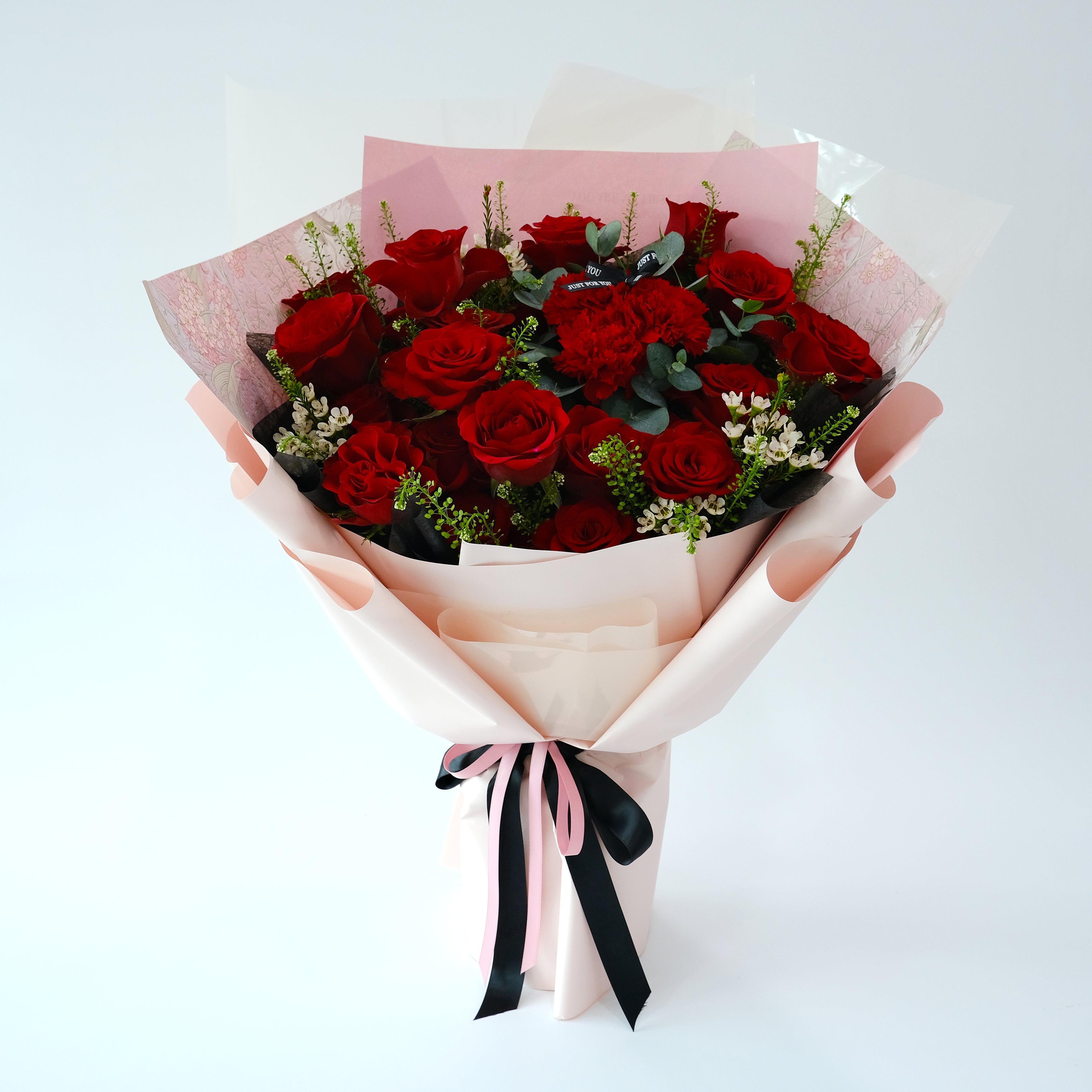 Bouquet of red roses wrapped in pink paper with a black ribbon on a white background