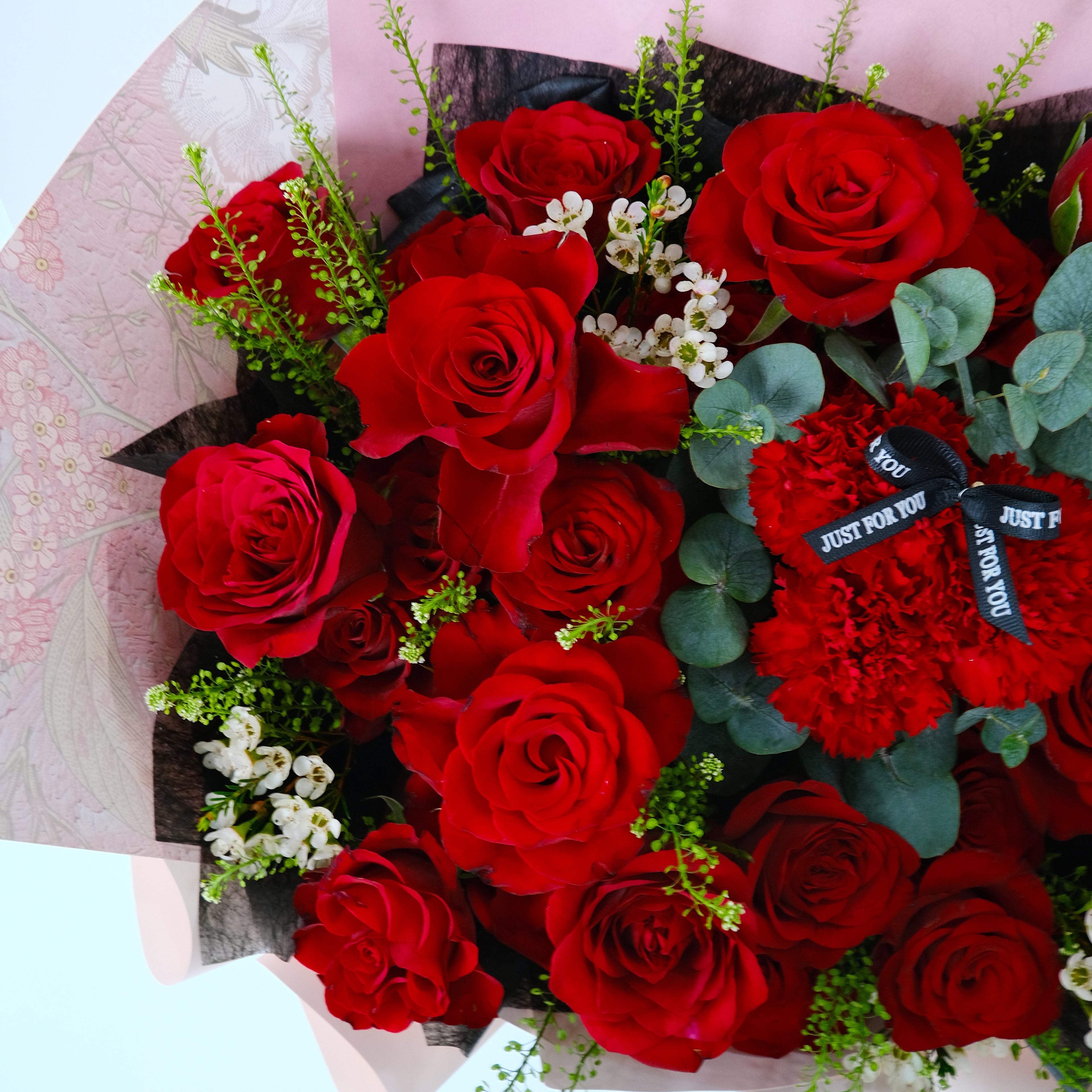 Bouquet of red roses with a decorative tag on a light pink background