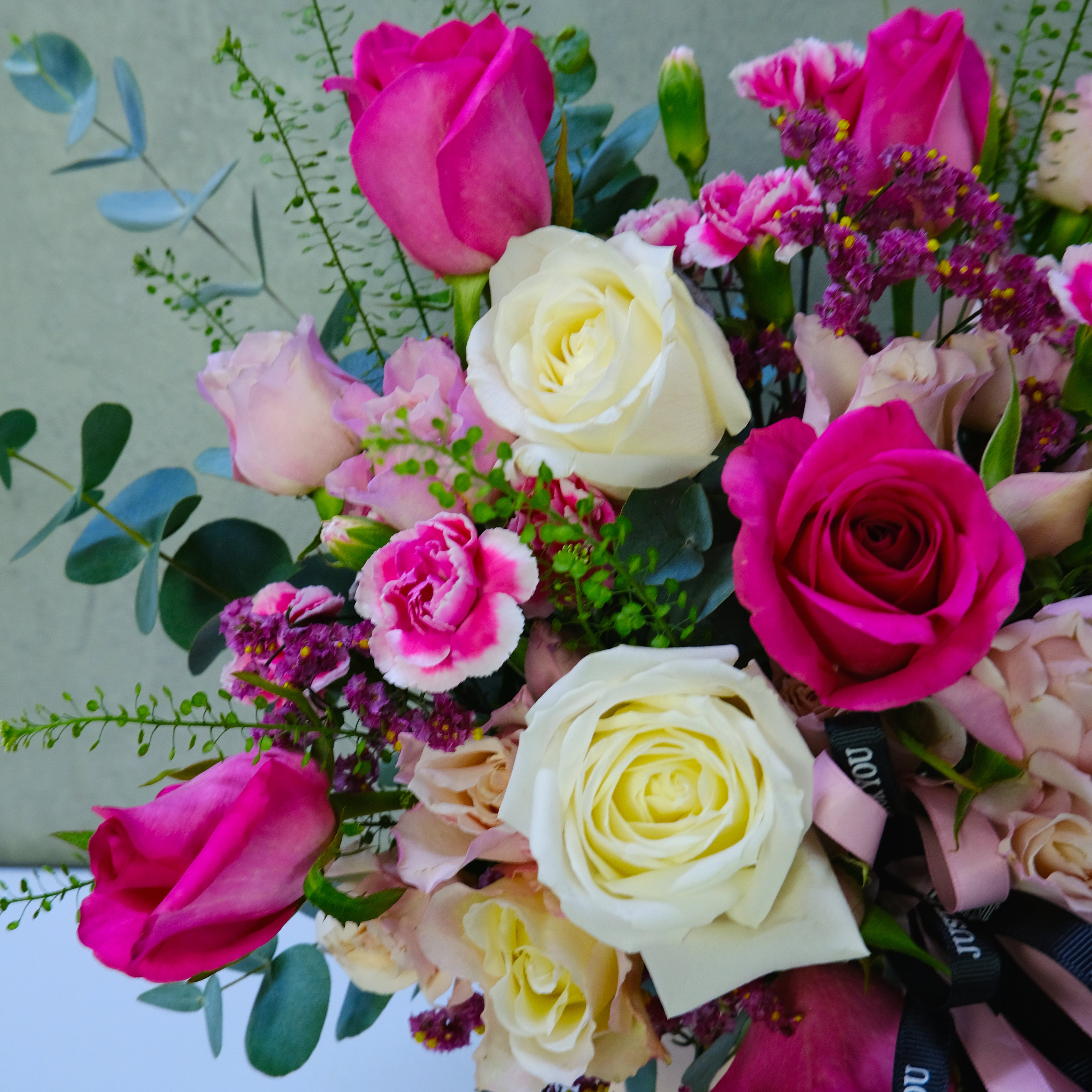 Bouquet of colorful flowers including pink, white, and purple roses on a light green background.